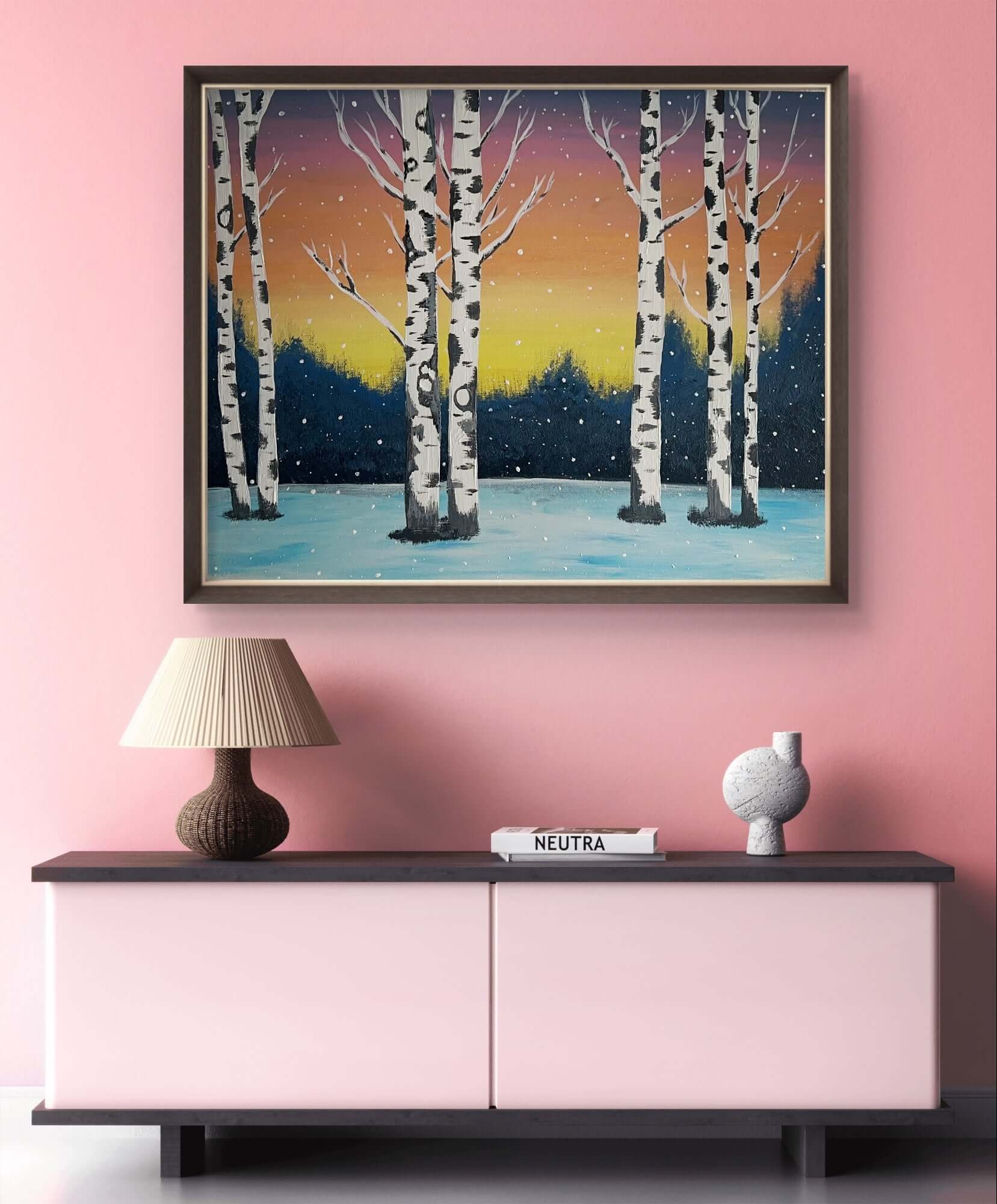 Acrylic painting of a winter forest scene with snow-covered trees and a sunset sky, displayed above a modern pink sideboard.