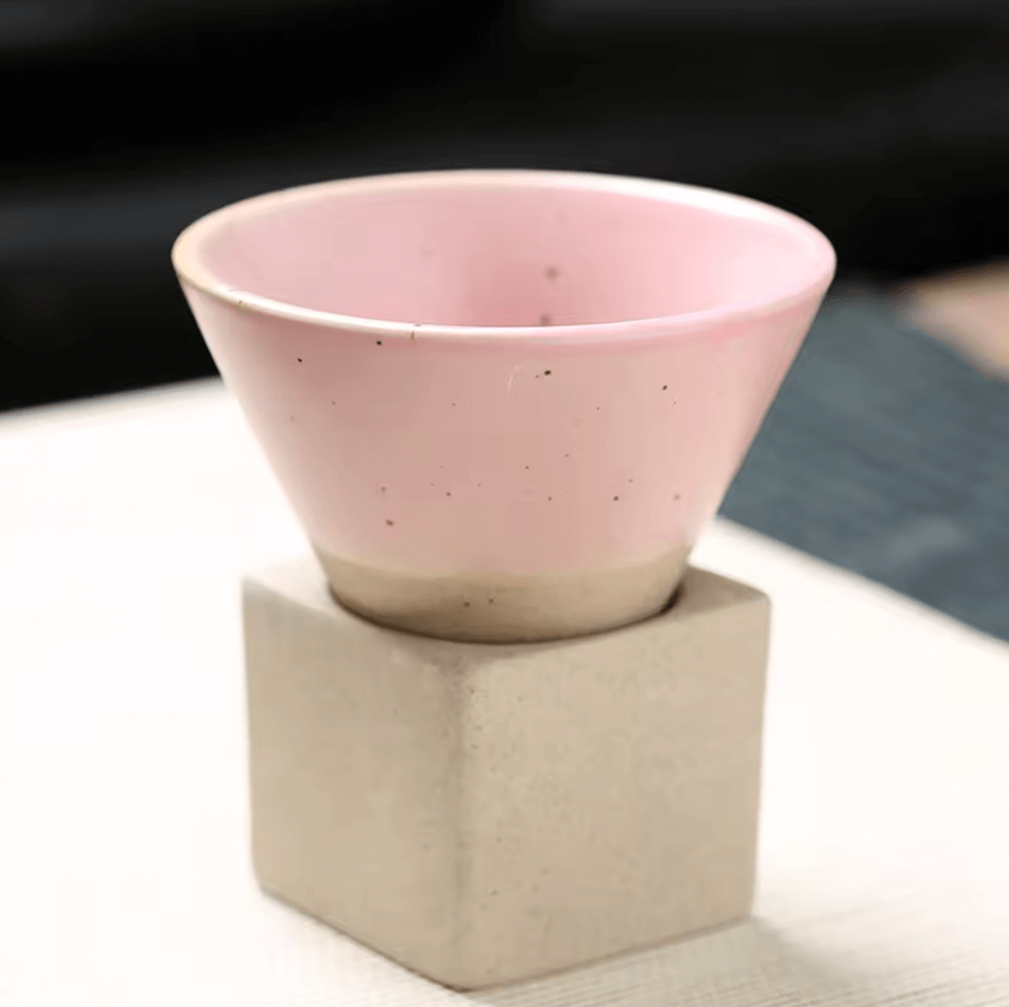 Handcrafted pink Japanese ceramic tea cup with unique conical design, blending tradition and modern style, placed on a solid base.