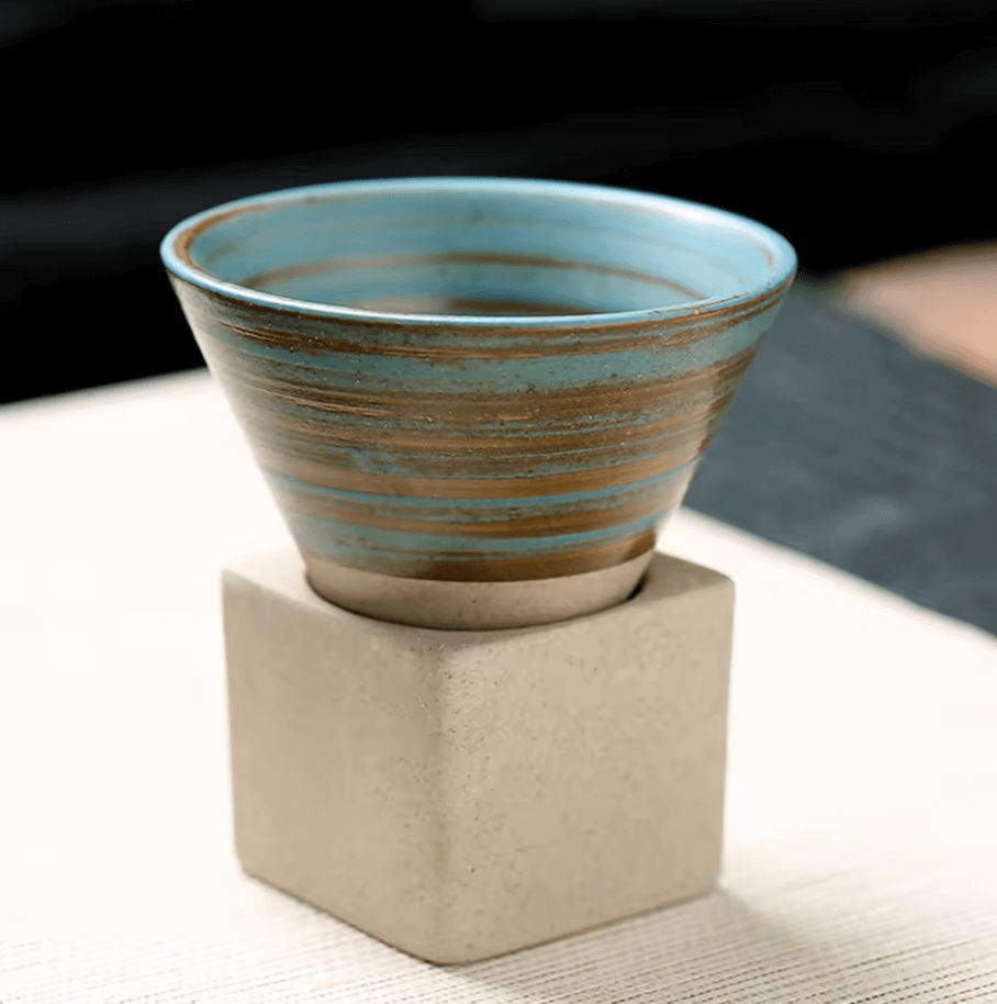Japanische Keramik-Teetasse in Kegelform mit einzigartigem Design und lebendigen Farben auf quadratischer Basis, perfekt für Tee.