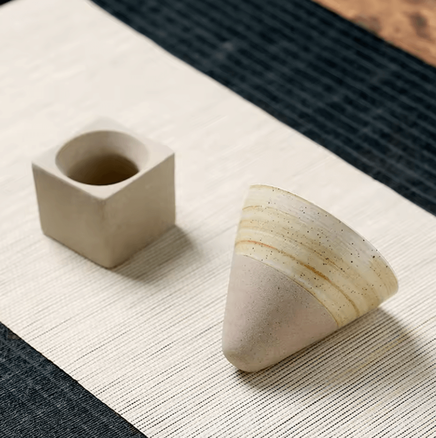 Modern ceramic teacup in unique conical shape with geometric design on a textured mat, ideal for Japanese tea rituals.
