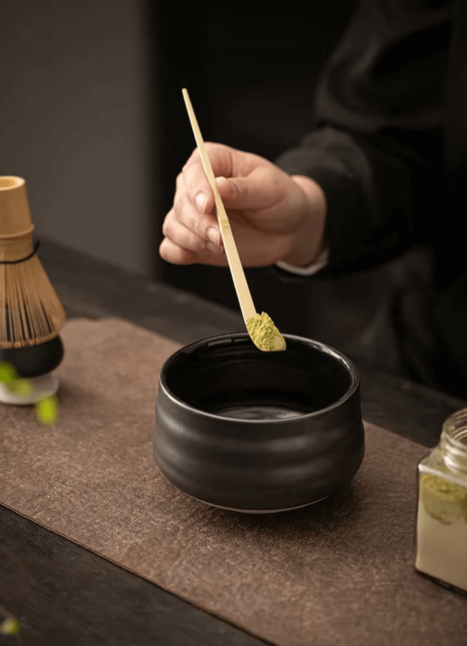 Person preparing matcha tea with traditional Japanese set, featuring a bamboo whisk and ceramic bowl.
