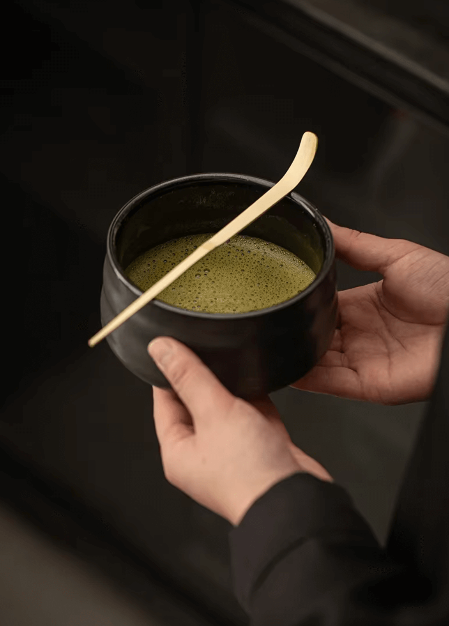 Person holding a traditional Japanese matcha bowl with matcha tea and bamboo whisk for tea ceremony.