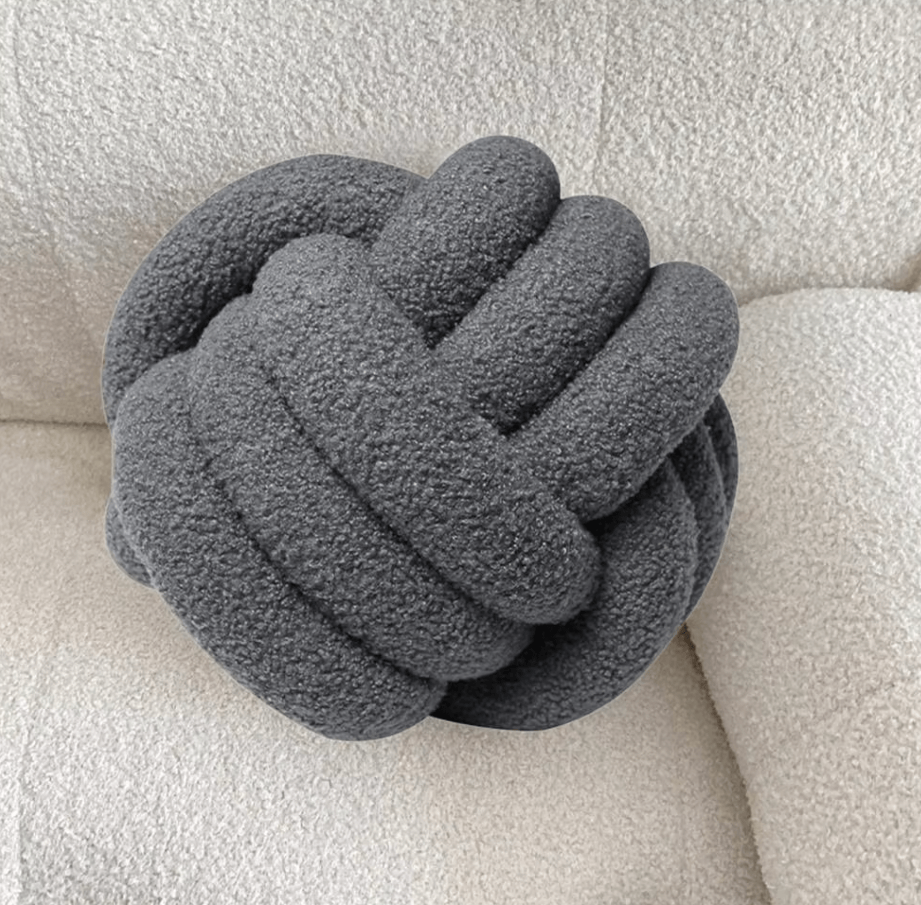 Gray handwoven knot cushion showcasing Scandinavian design and soft Sherpa wool for comfort on a beige sofa.