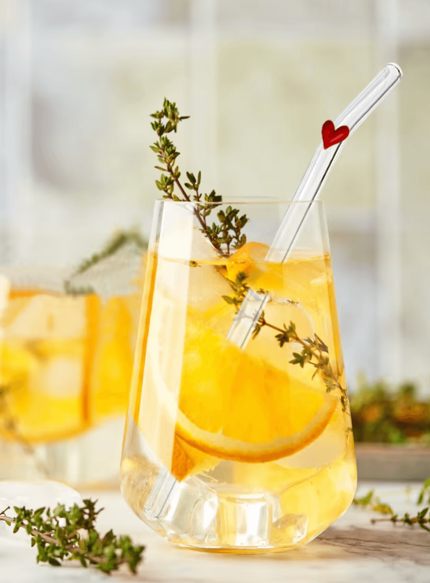 Glass with orange slices and herbs, featuring a stylish Pure Sip glass straw for eco-friendly drinking.