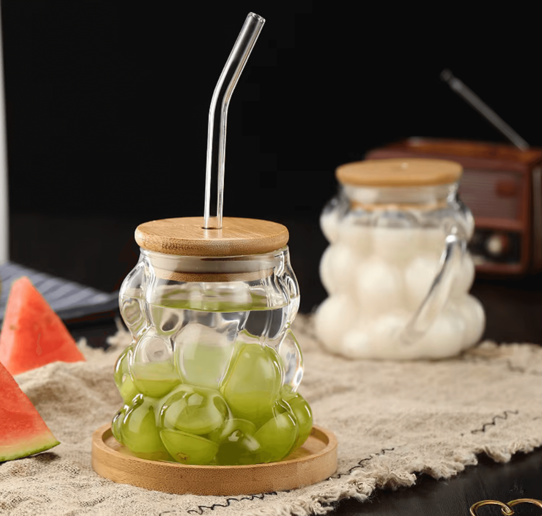Stylish glass tumblers with bubble design, bamboo lids, and straws, ideal for serving drinks like juice or water, on a rustic table.