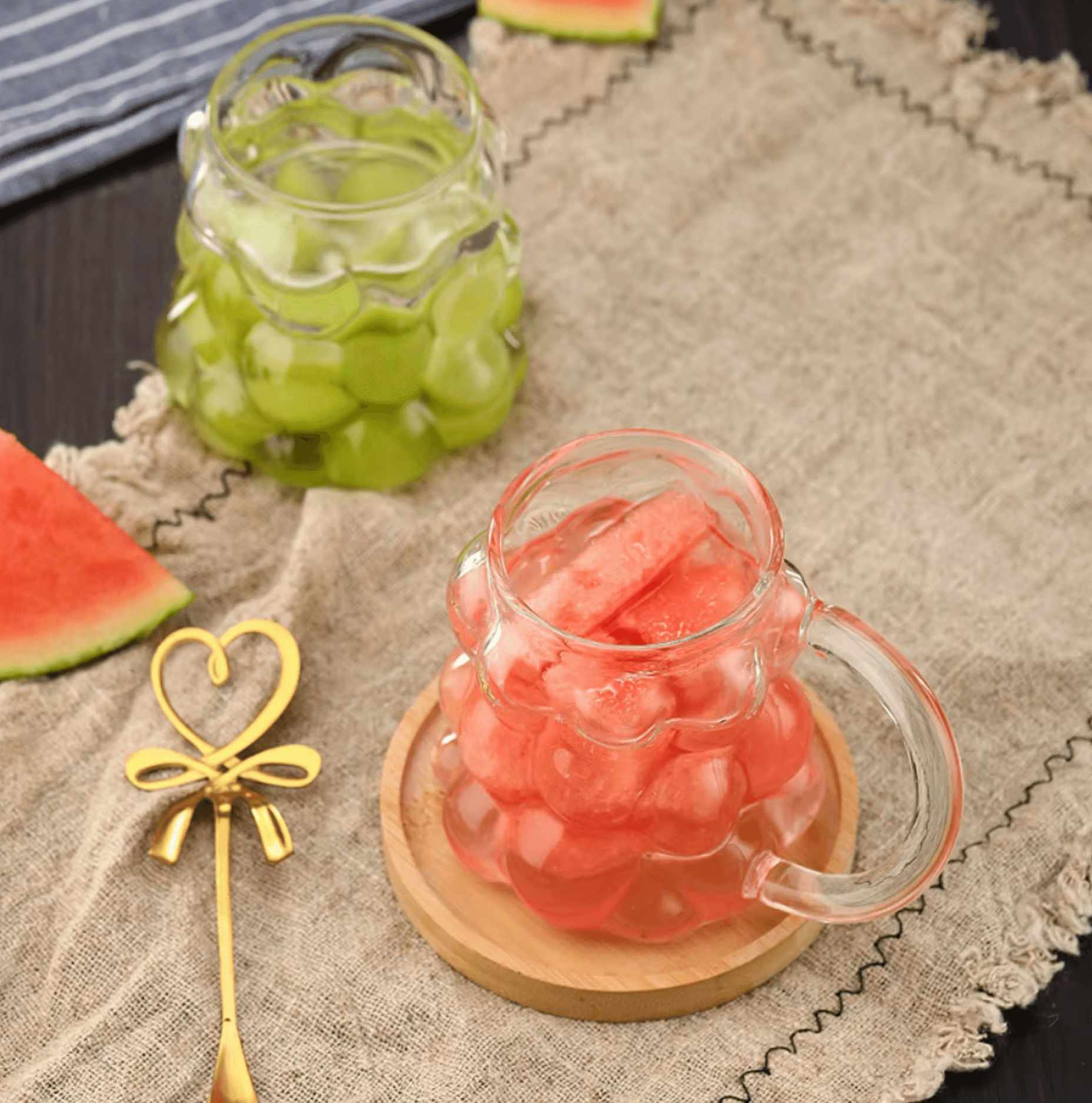 Unique textured glass mugs filled with refreshing green and pink beverages, placed on a rustic cloth with a decorative spoon.