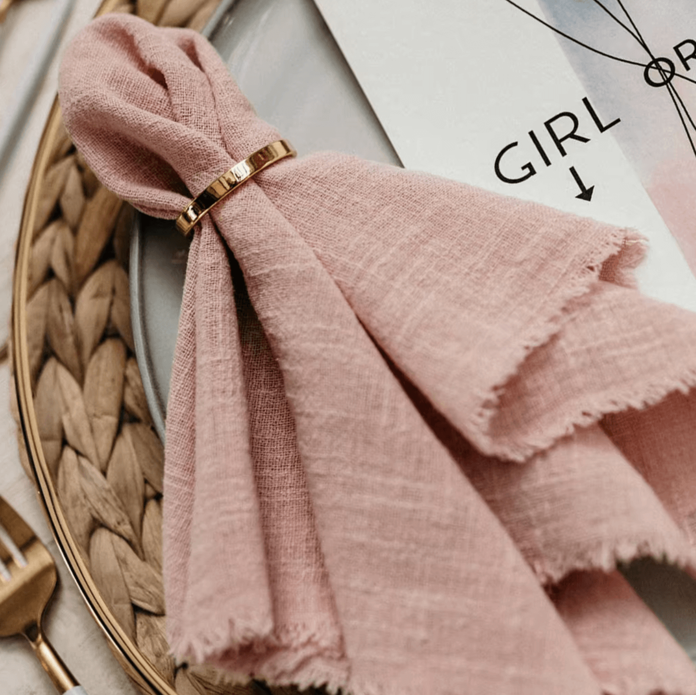 Pink napkin with elegant gold napkin ring on a dining plate, enhancing luxury table setting.
