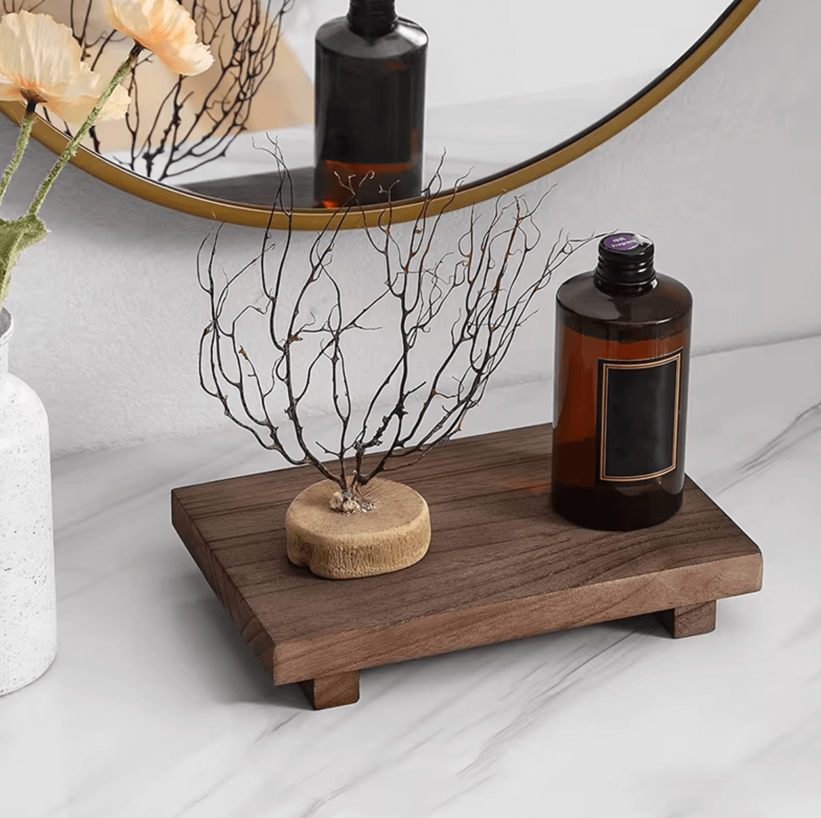 Eichenholz-Tablett dekoriert mit Flasche und Zweigen vor einem runden Spiegel auf einem Marmortisch, natürlicher Charme, Retro-Design.