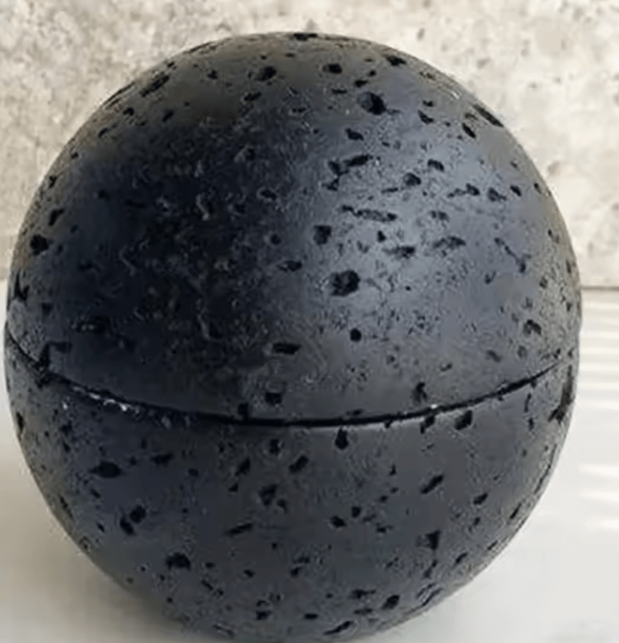 Black volcanic stone sphere with textured surface on a flat background.