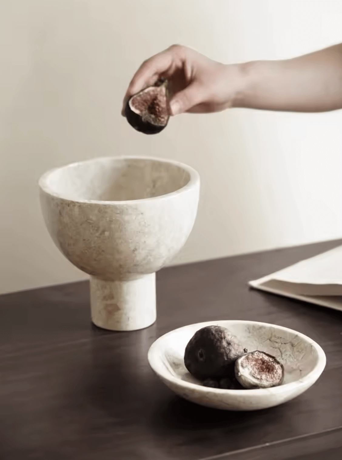 French-style luxury marble bowls on a table, with a hand placing figs as an elegant, functional decor piece.