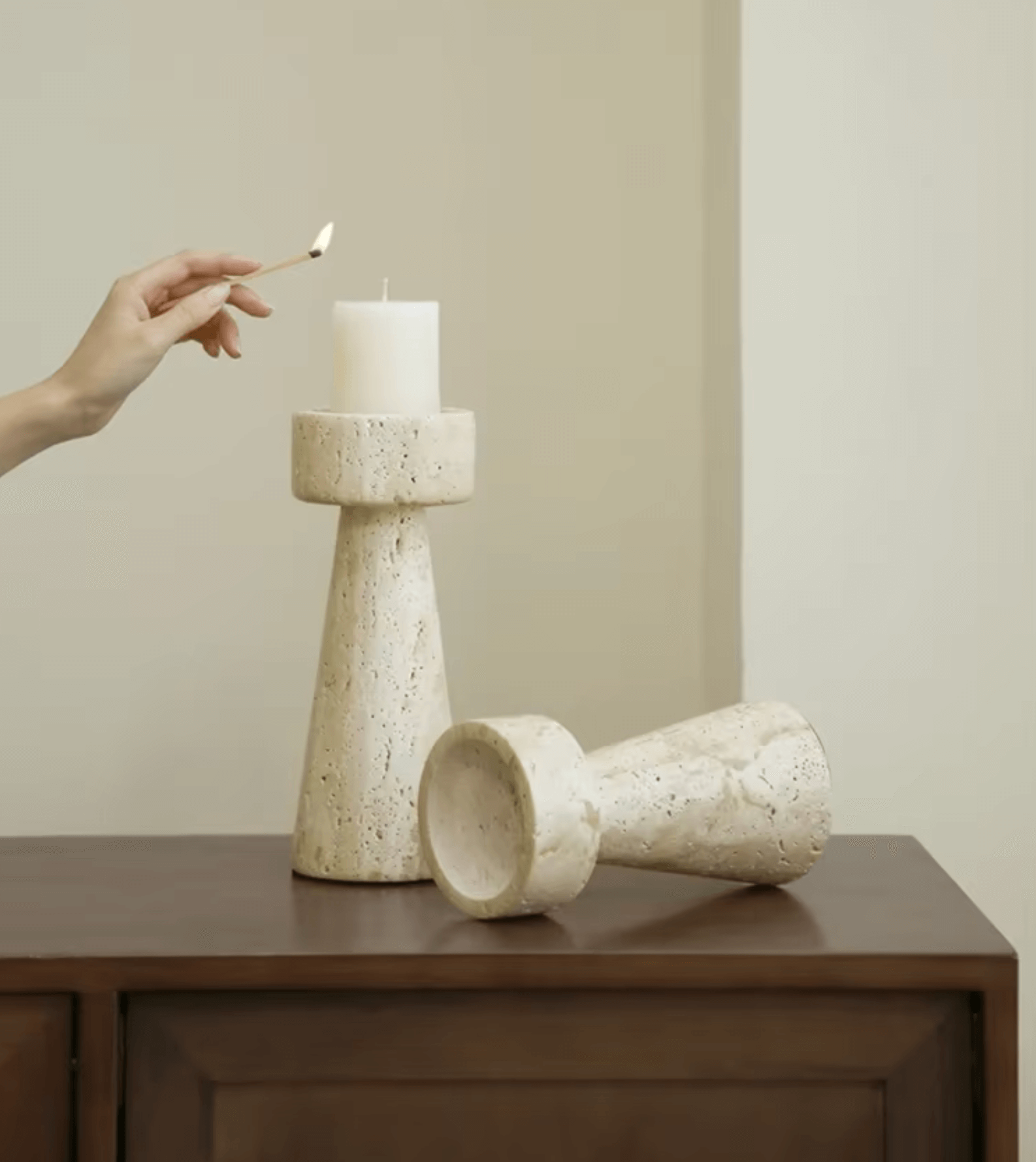 Hand lighting a candle on a travertine marble holder, showcasing elegant natural design on a wooden table.
