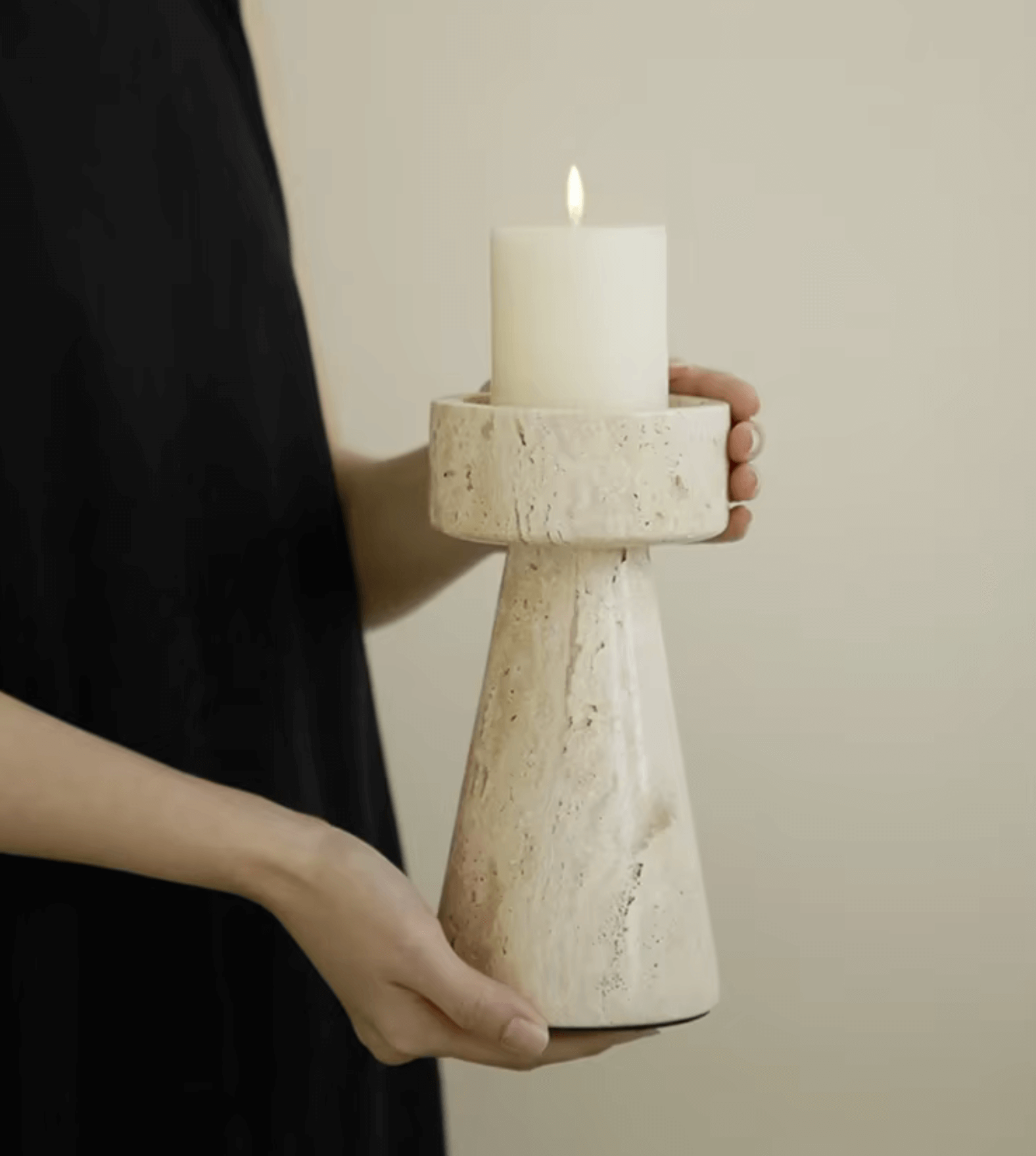 Hand holding a travertine marble candle holder with a lit candle, showcasing timeless elegance and natural stone design.