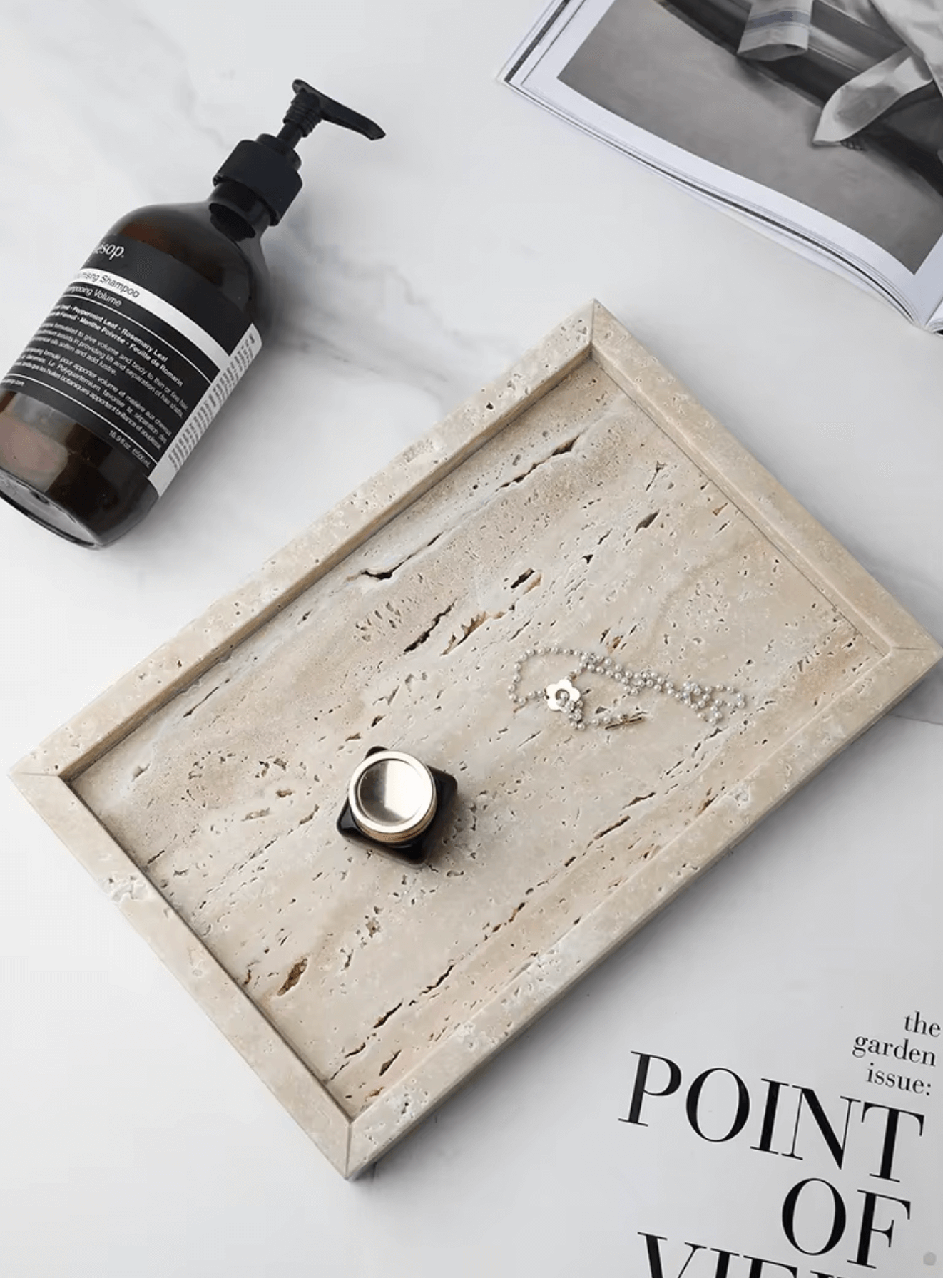 Minimalistisches Marmor-Tablett aus Travertin mit Luxus-Akzenten, umgeben von Schmuck und Flasche auf einem Magazin.