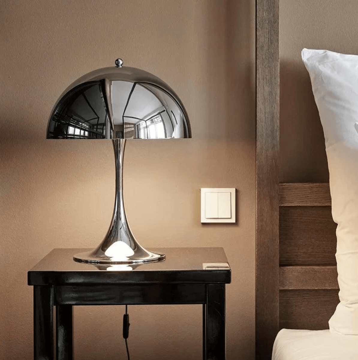 Chrome mushroom table lamp on nightstand, Italian minimalist design, illuminating elegant bedroom setting.