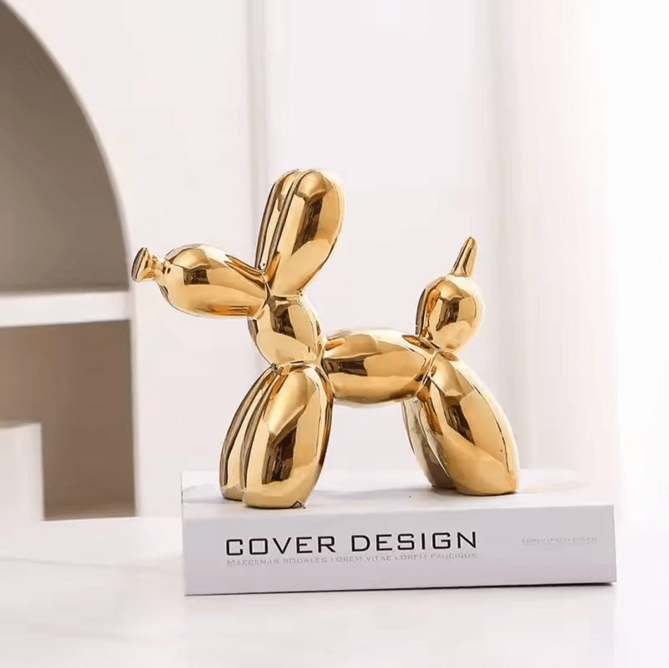 Gold ceramic balloon dog sculpture on a book, blending nostalgia with modern design.