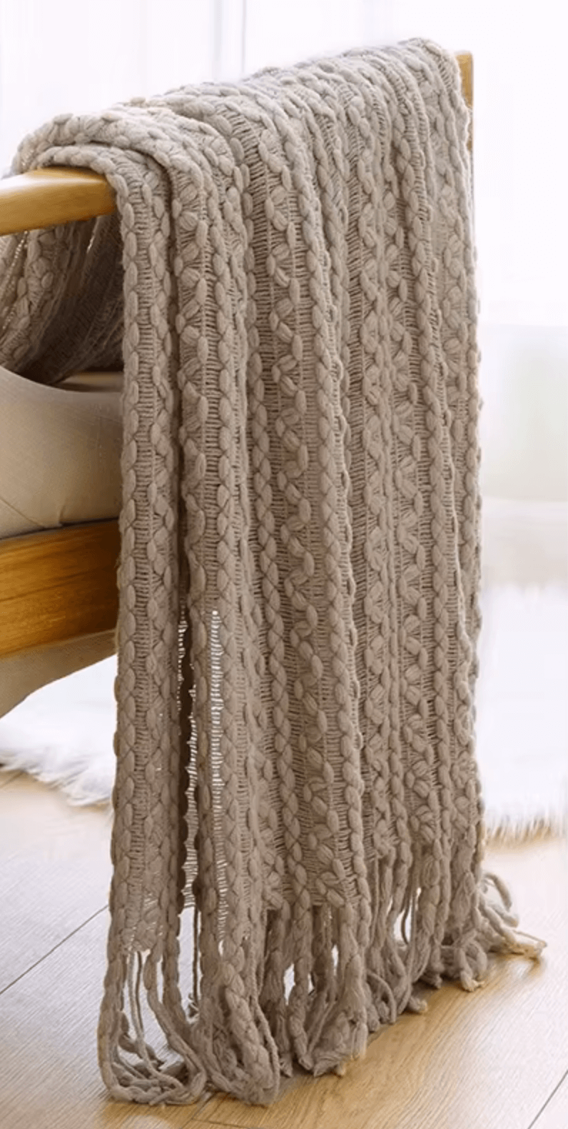 Boho-Strickdecke mit Quasten in beige, handgefertigt, luxuriöses Vintage-Design auf Holzbett, idealer Sofabegleiter für gemütliche Stunden.