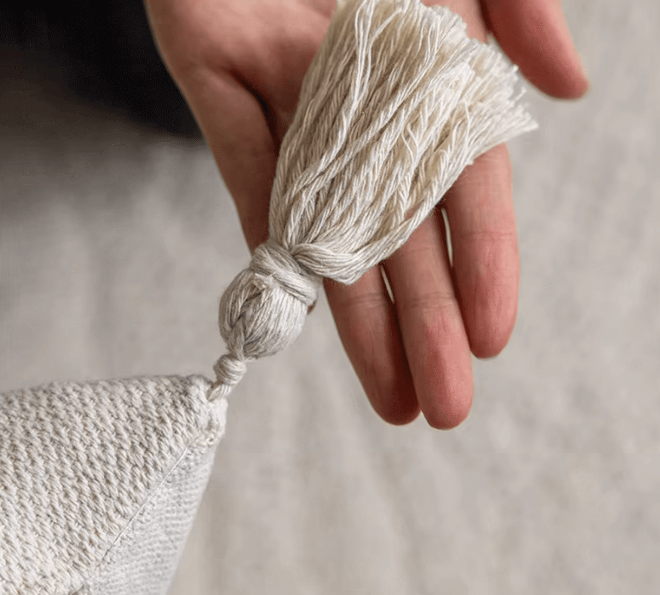 Hand holding a beige tassel of a Nordic Retro Cushion Cover with tufting detail.