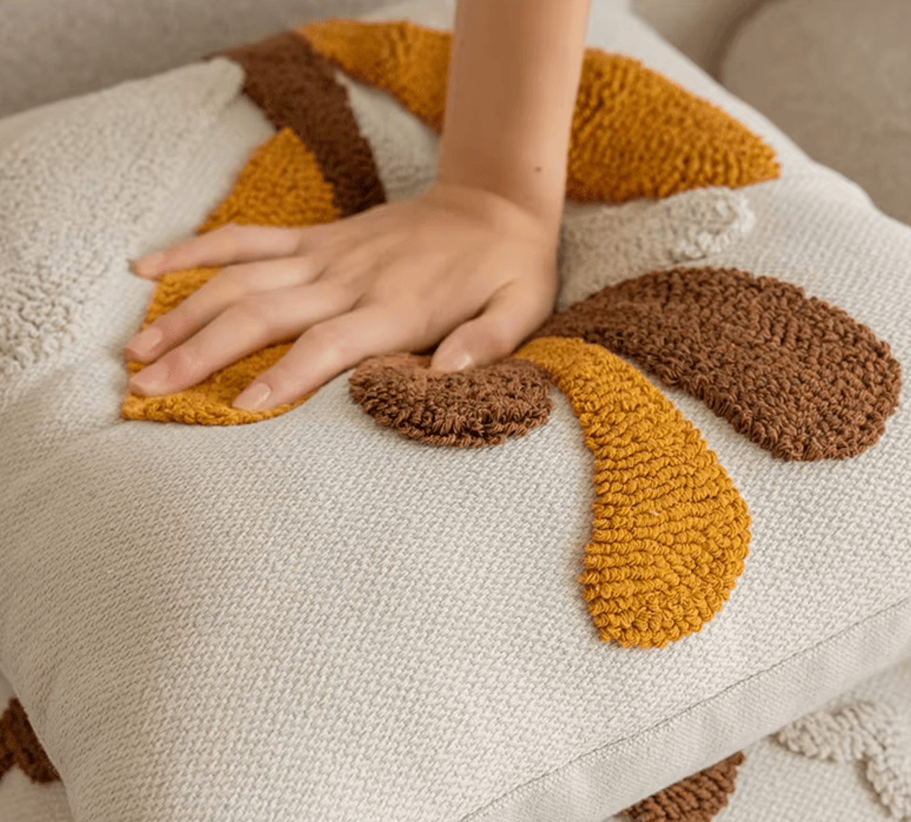 Hand touching Nordic Retro Kissenbezug with geometric tufting in warm yellow-brown on a sofa for a cozy Scandinavian style.