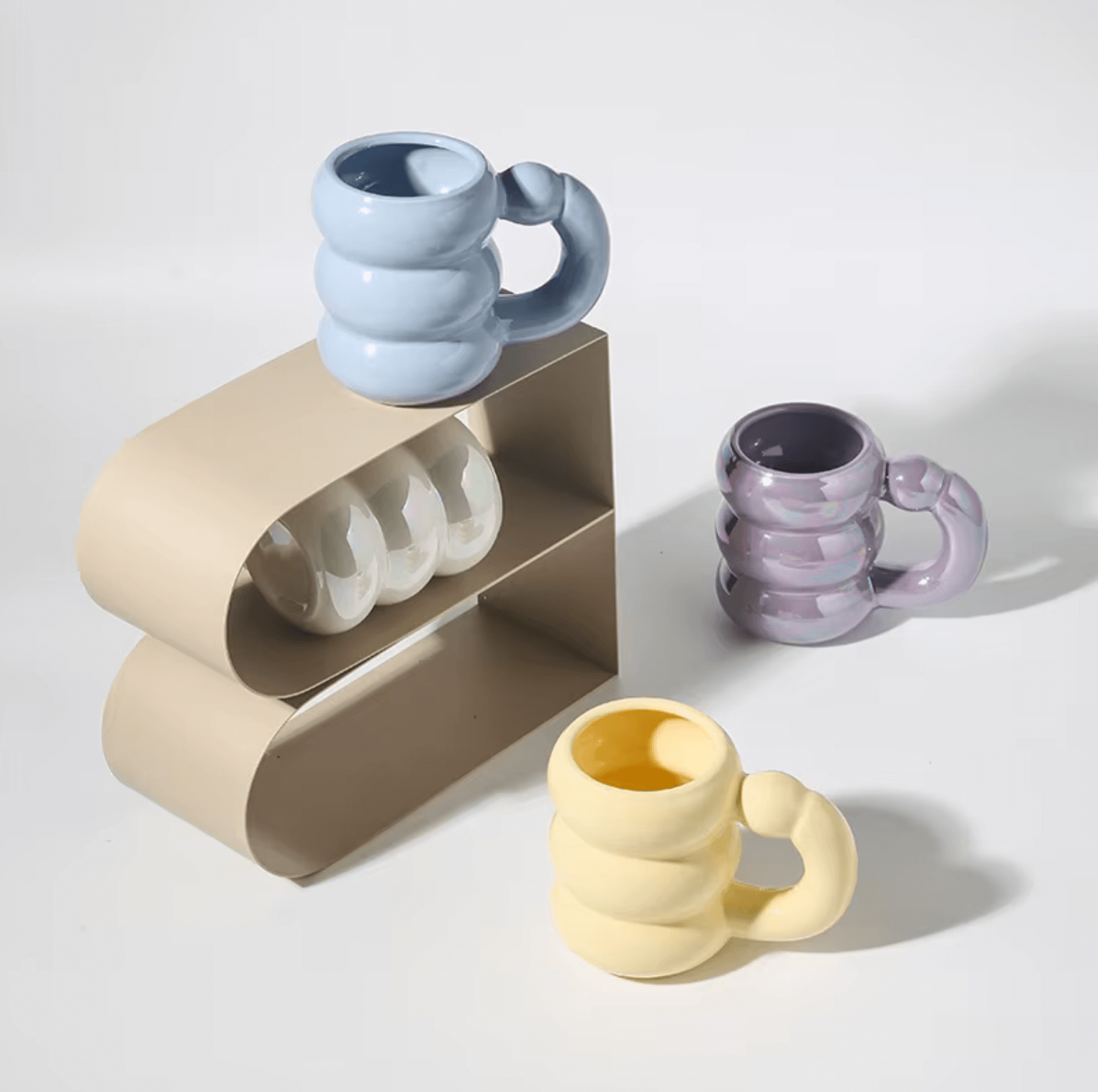 Colorful Korean design mugs with unique spiral handles displayed on a modern beige shelf, featuring pastel shades of blue, yellow, and purple.