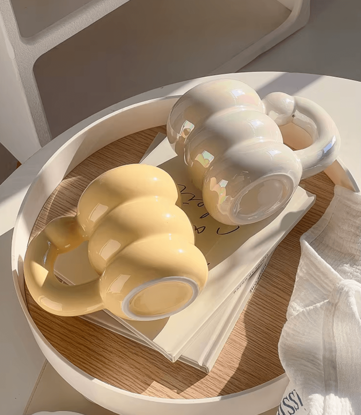 Two Spring Bloom mugs with modern Korean design, in yellow and white, placed on a round wooden tray under soft lighting.