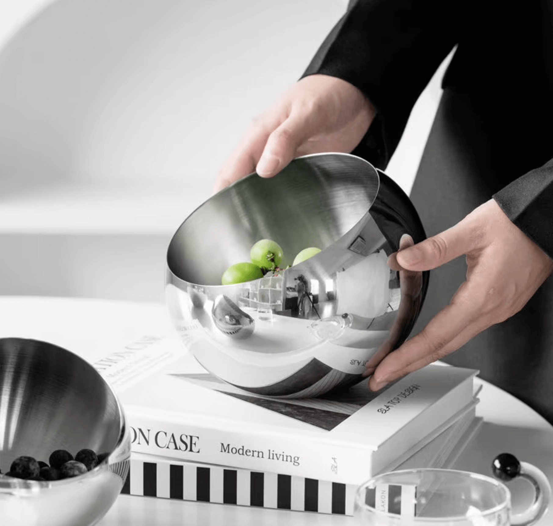 Person holding a modern, minimalist stainless steel bowl with green apples inside, placed on books, ideal for stylish living spaces.