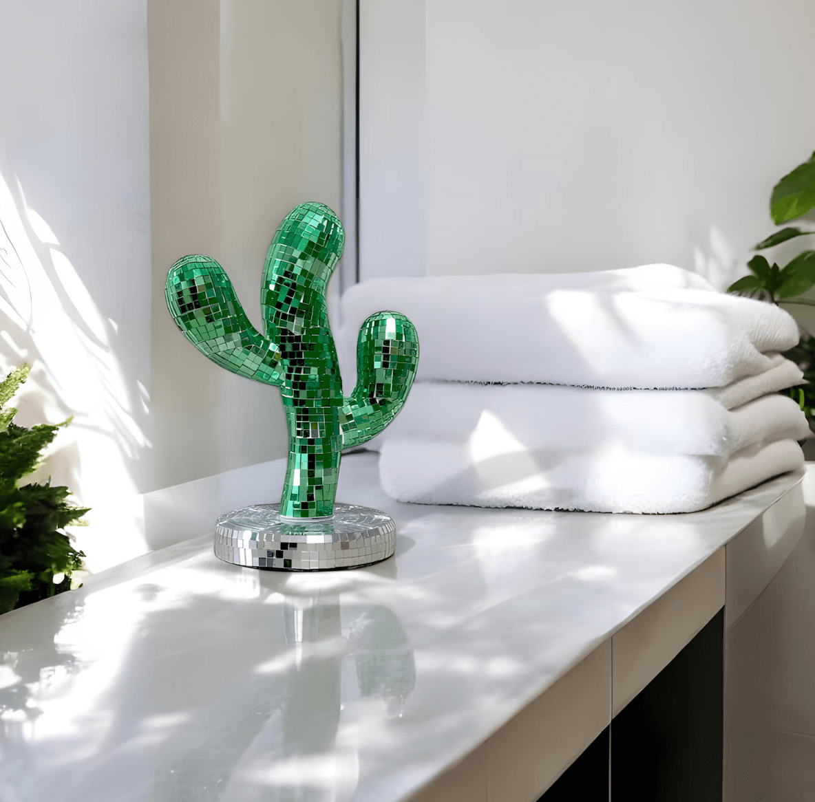 Shiny disco-cactus statue on a bathroom counter, adding a retro charm with its reflecting surface beside fluffy white towels.