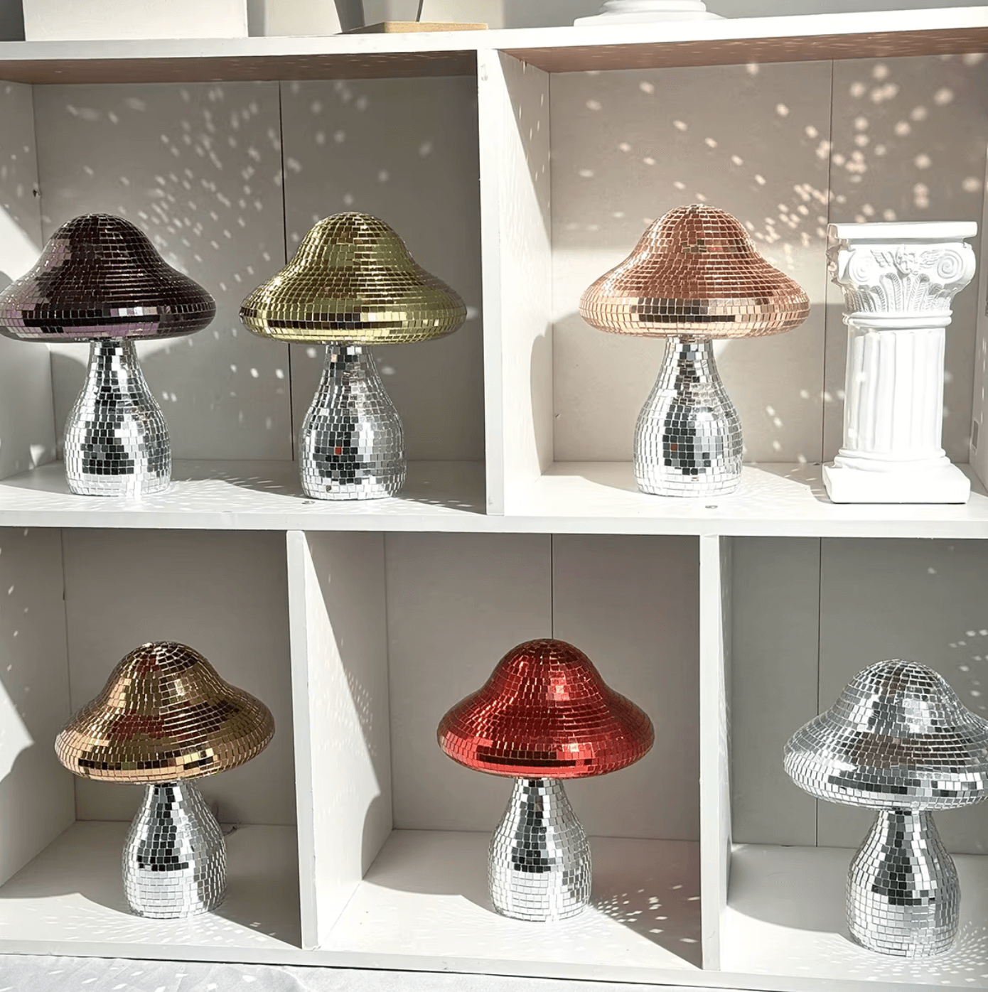 Reflective disco mushroom decor in silver, gold, and rose gold displayed on shelves, creating magical light patterns in a room.