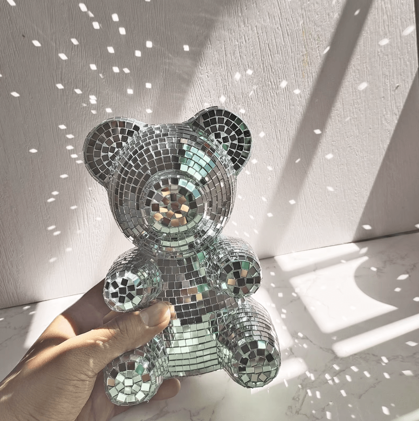 Disco-Bär, retro-style decor, shimmering bear with mirror tiles, reflecting light, perfect home decor centerpiece, hand holding bear.