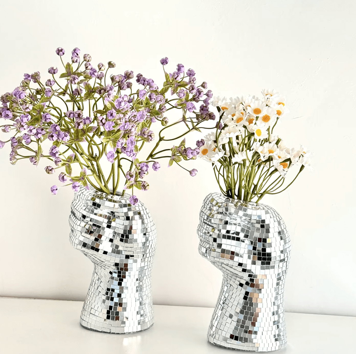 Silver disco hand-shaped vases with mirrored tiles, holding purple and white flowers, showcasing retro and modern decor style.