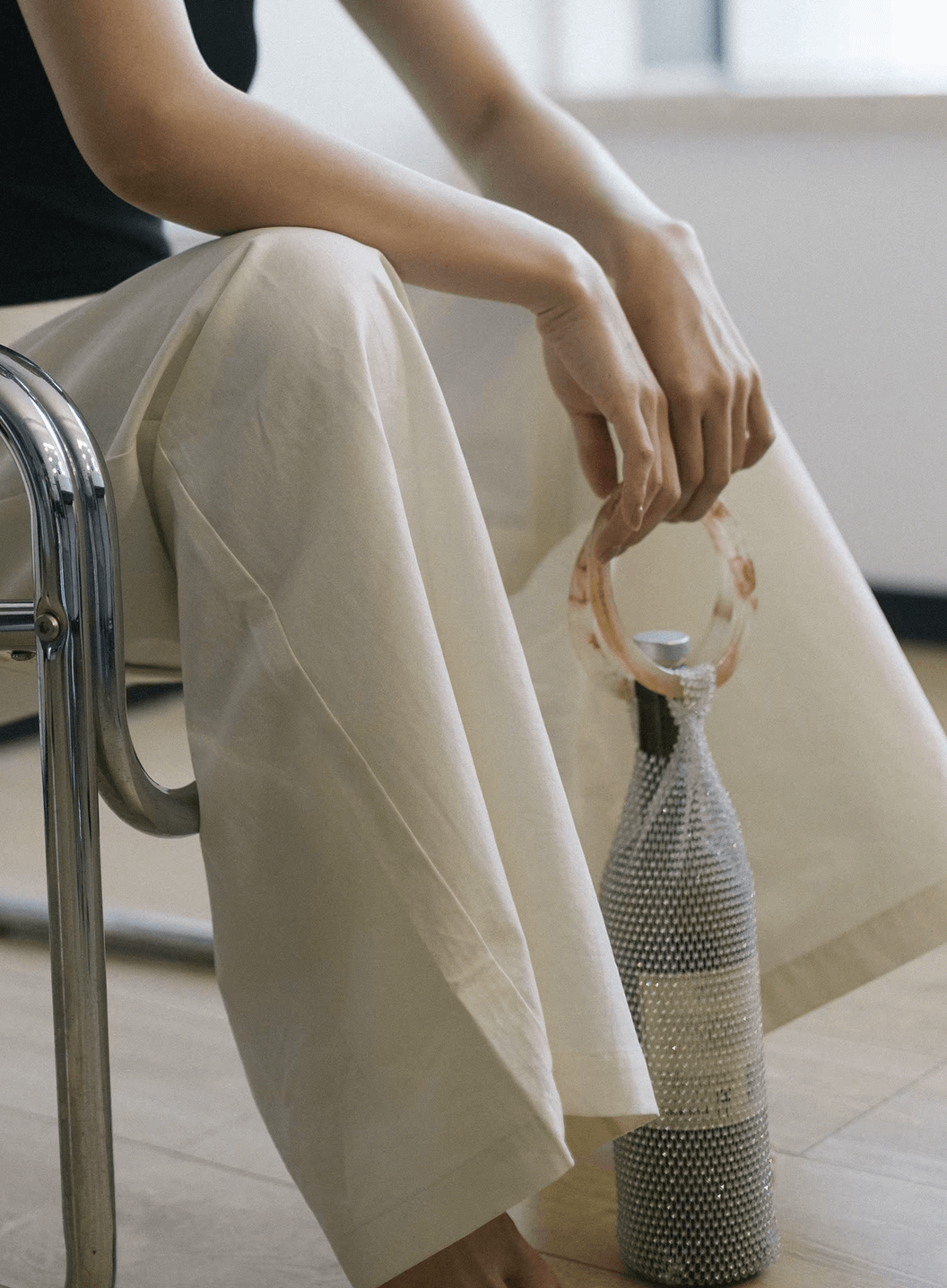 Person sitting with handwoven bottle bag featuring elegant design and Czech diamond handle, ideal for stylishly carrying beverages.