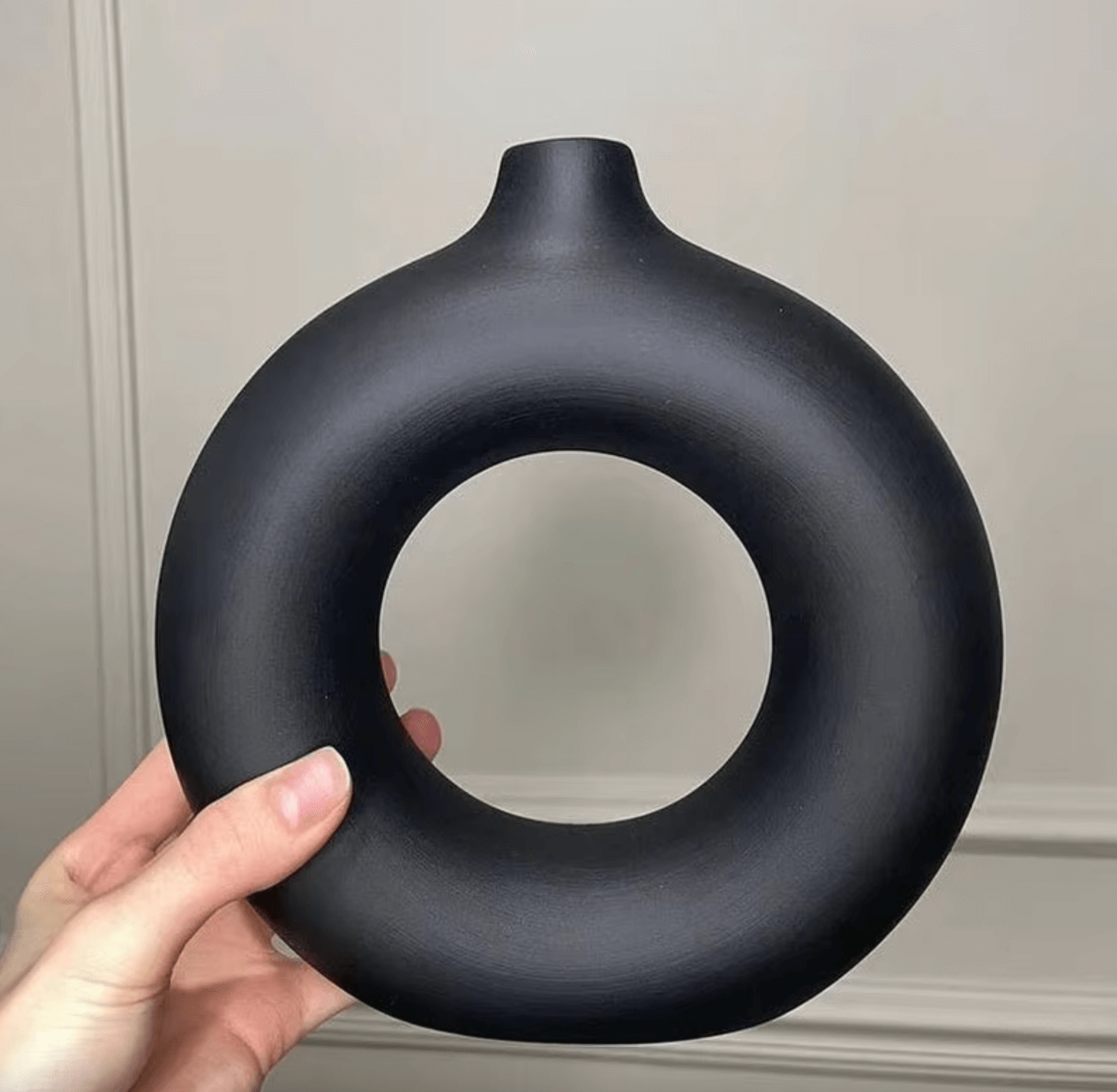 Elegant black circular Nordic vase with minimalist design, held by a hand, perfect for adding Scandinavian style to home decor.