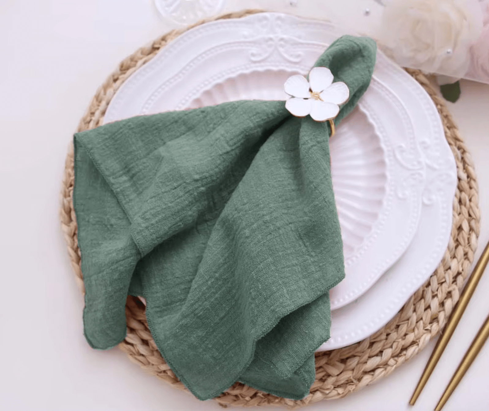 Green cotton napkin elegantly folded on a white plate with a floral ring, showcasing sustainable table decor for weddings and dinners.