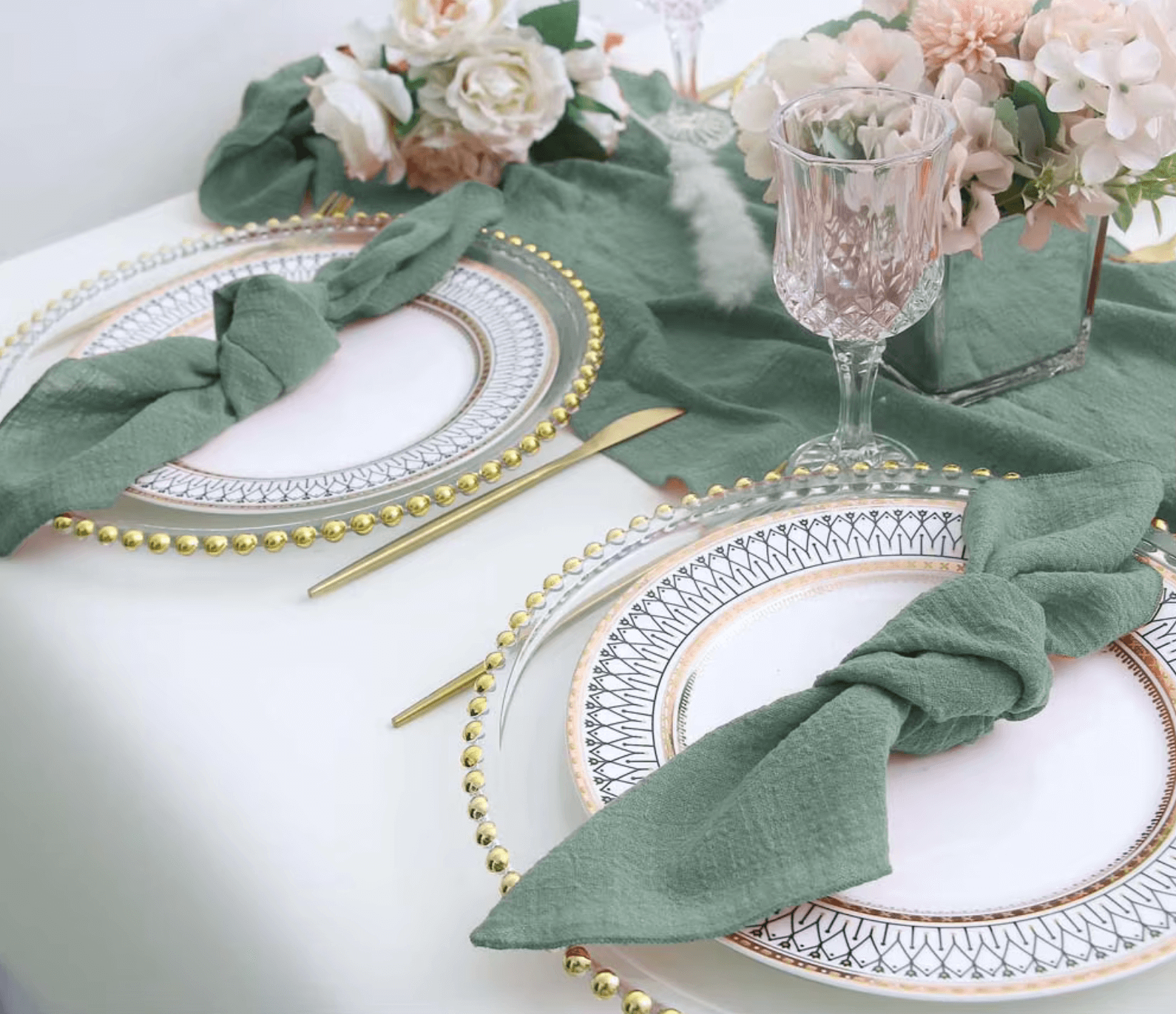 Elegant table setting with green cotton napkins, gold-rimmed plates, crystal glassware, and floral centerpiece for dinner party.