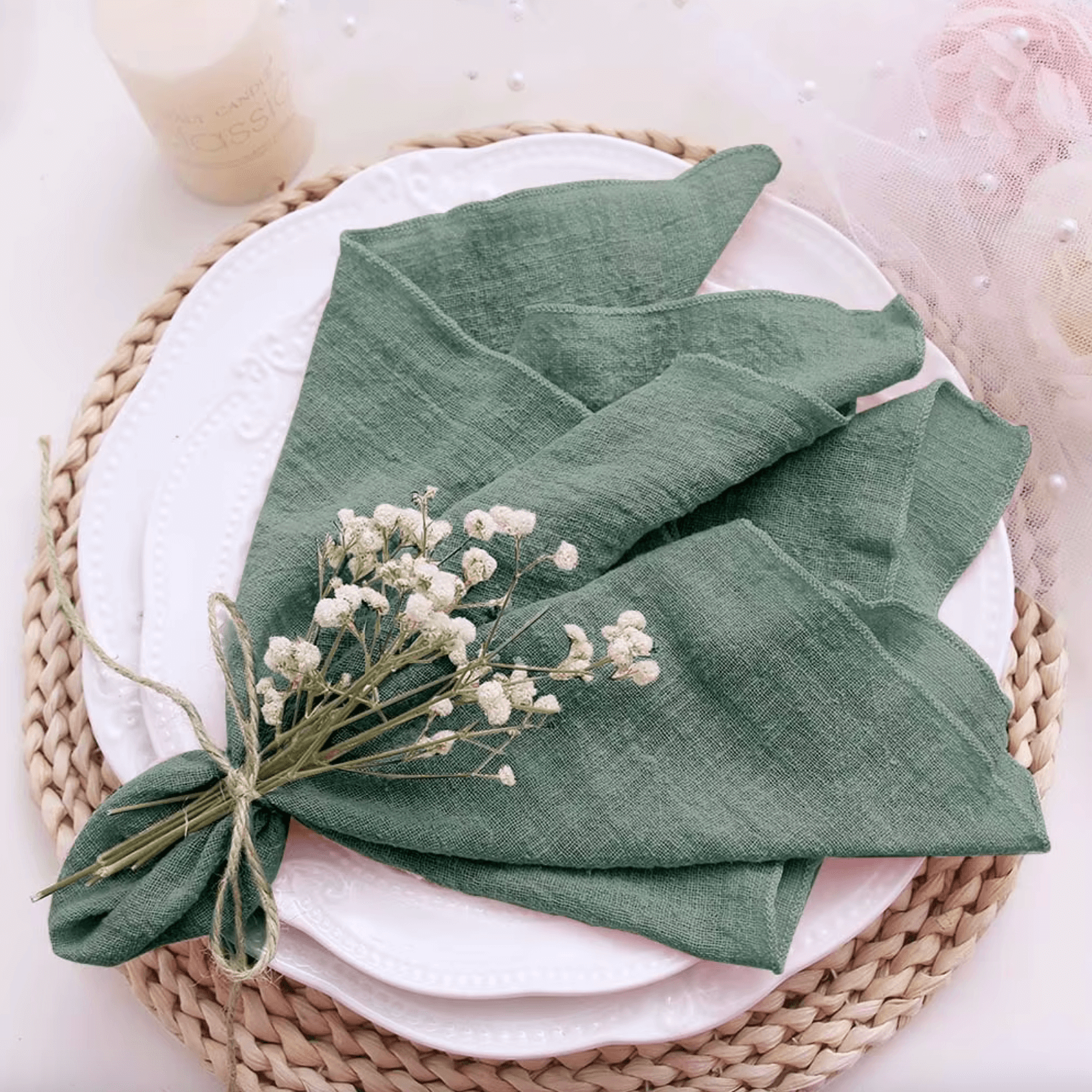 Green cotton napkin elegantly folded on a white plate, adorned with delicate white flowers. Perfect for sustainable dining.