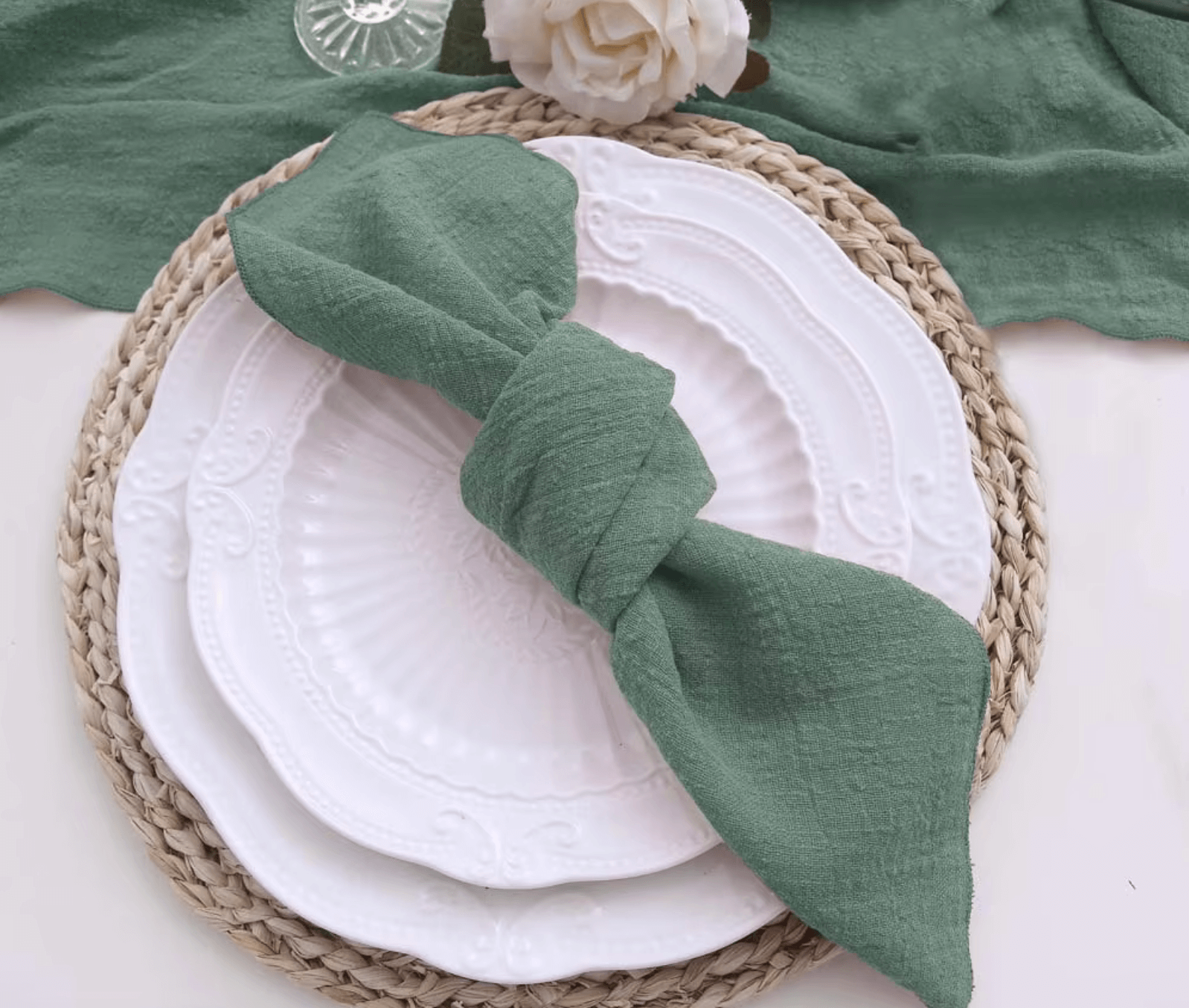 Elegant table setting with green cotton napkin on white plates, showcasing sustainable dining aesthetics.