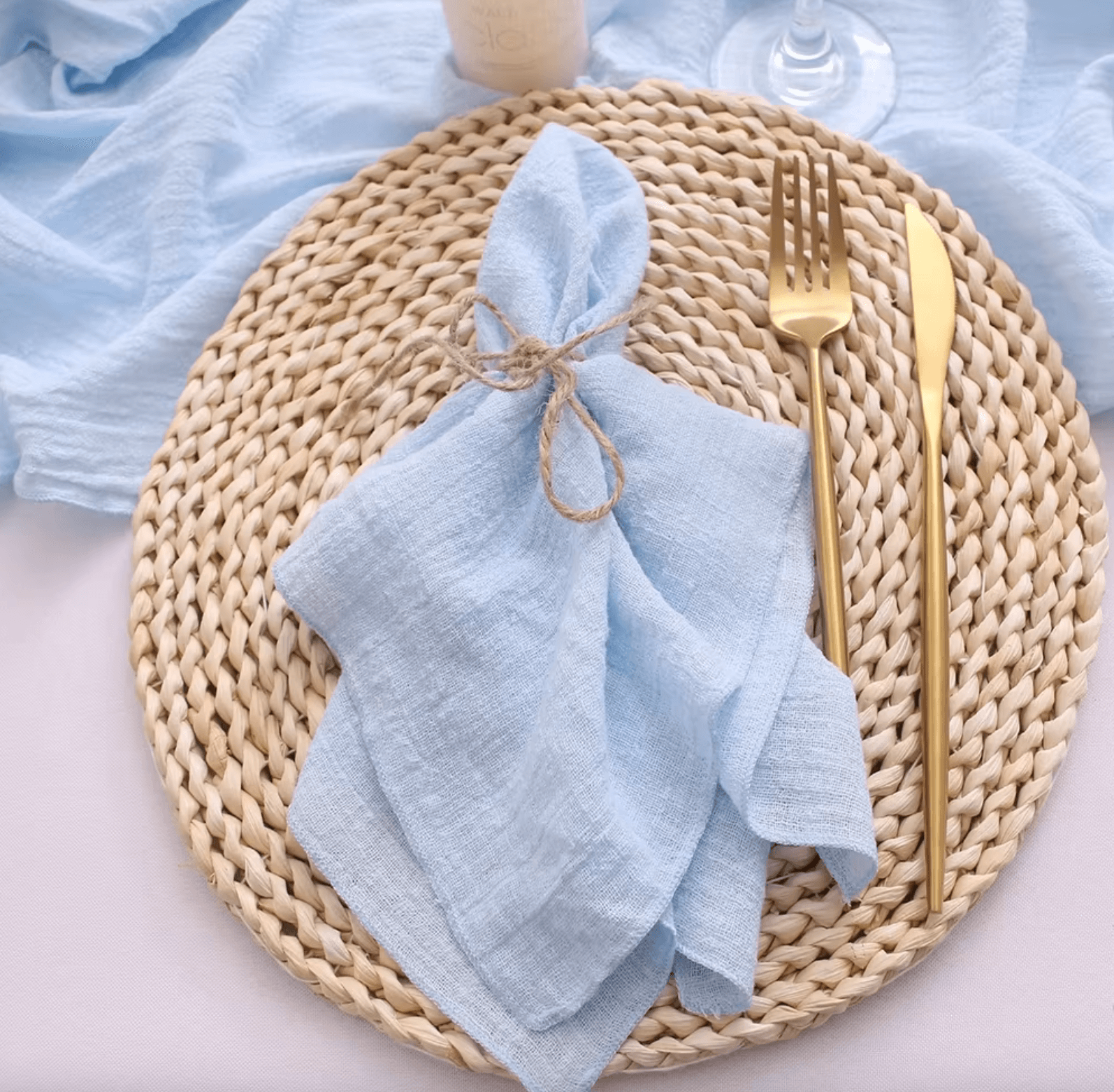 Light blue cotton napkin on a woven placemat with gold cutlery, showcasing elegance and sustainability for a stylish table setting.