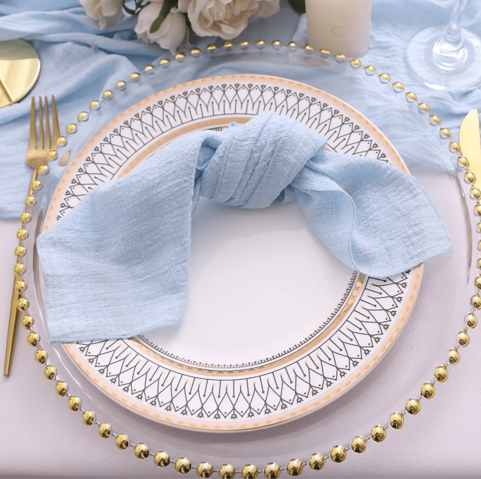 Elegantly folded blue cotton napkin on decorative dinner plate with gold cutlery on a stylishly set table.