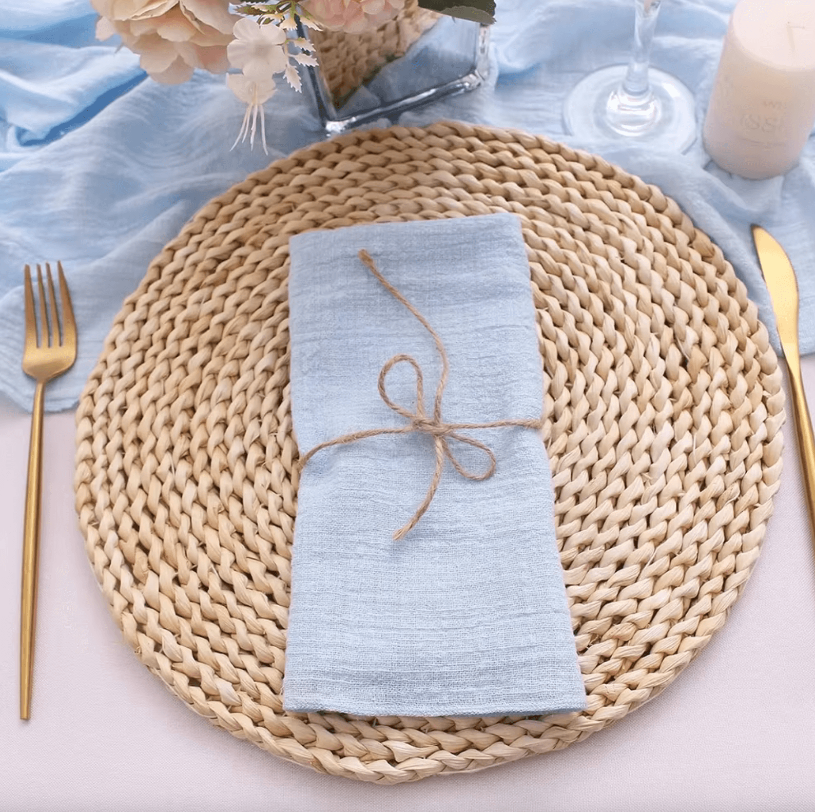 Baumwoll-Serviette in Blau auf geflochtenem Platzdeckchen, elegant gedeckter Tisch mit Besteck und Dekoration.