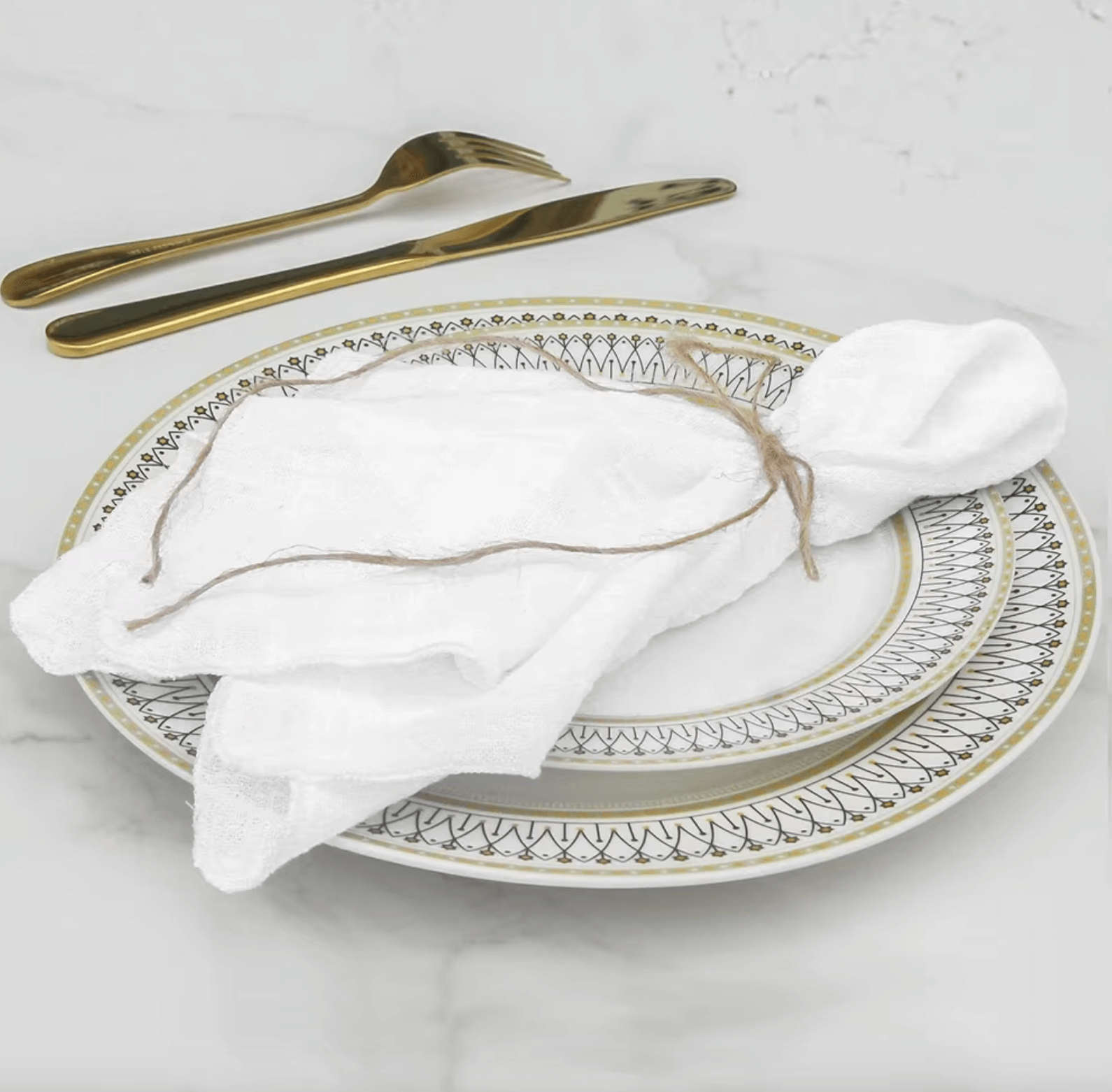 Elegante weiße Baumwoll-Serviette auf dekorativem Porzellanteller mit goldenem Besteck, ideal für nachhaltige Tischdekoration.