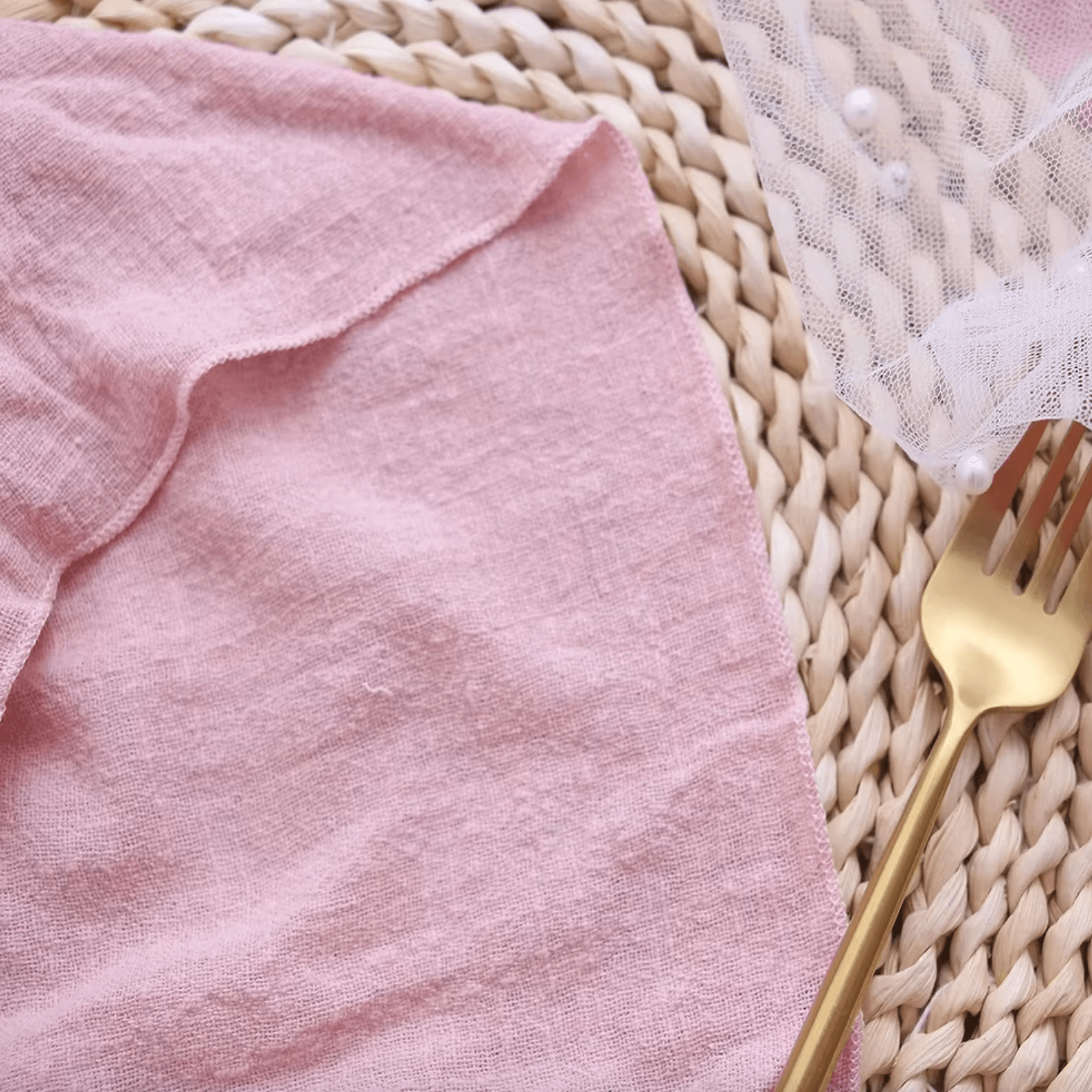 Pink cotton napkin with gold fork on a textured round placemat, showcasing elegant and sustainable table setting.