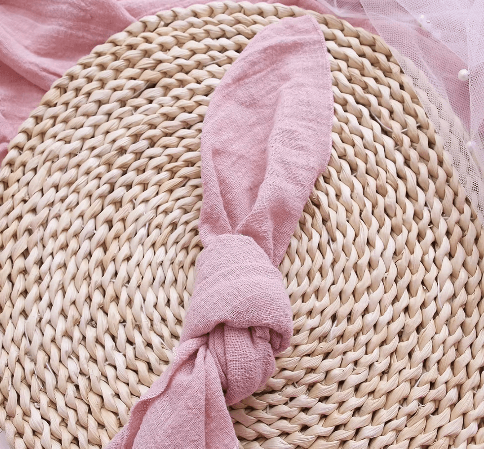 Elegant pink cotton napkin elegantly folded on a rustic woven placemat.