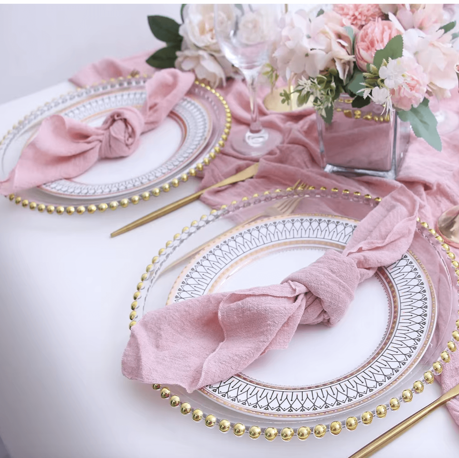 Elegant table setting with pink cotton napkins, gold-rimmed plates, and floral centerpiece, showcasing eco-friendly dining decor.