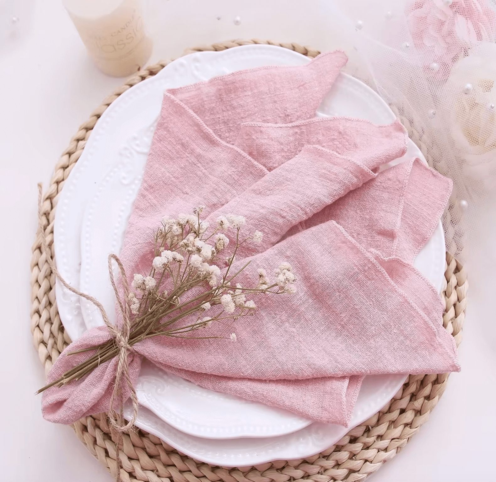 Elegant pink cotton napkin with floral decoration on a white plate and woven charger, showcasing sustainability and style.