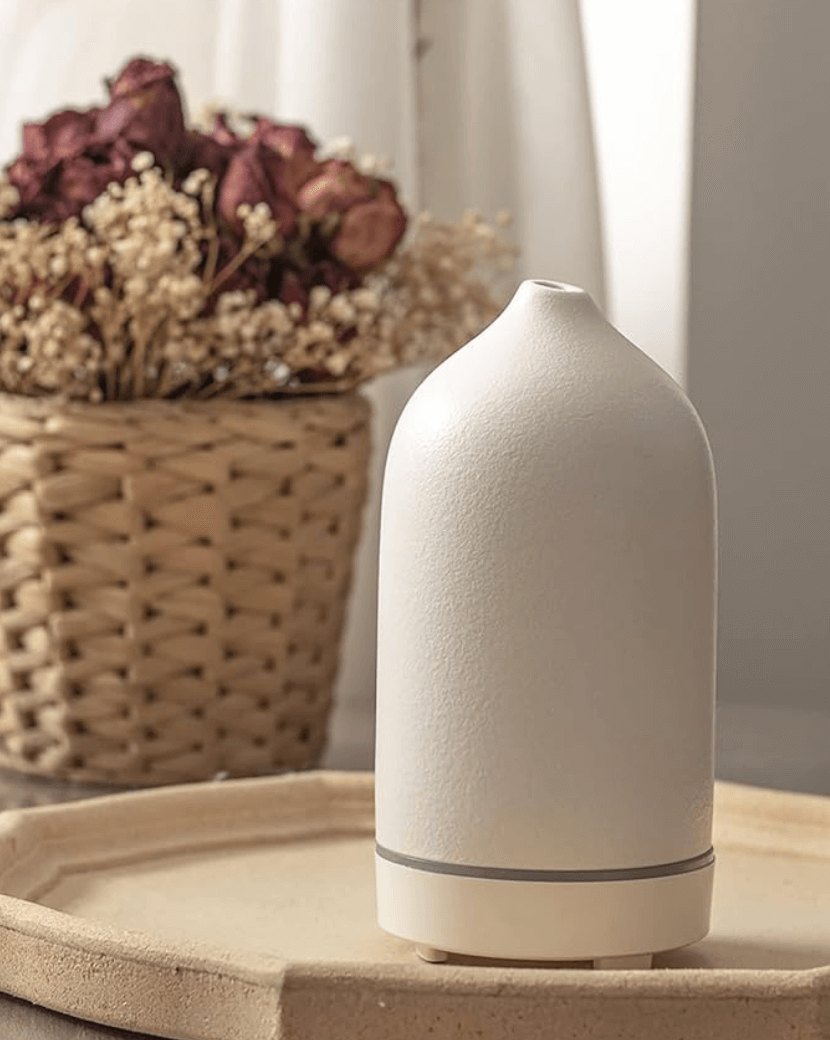 Modern white ultrasonic aromatherapy diffuser for home and office relaxation, shown on a tray near decorative flowers.