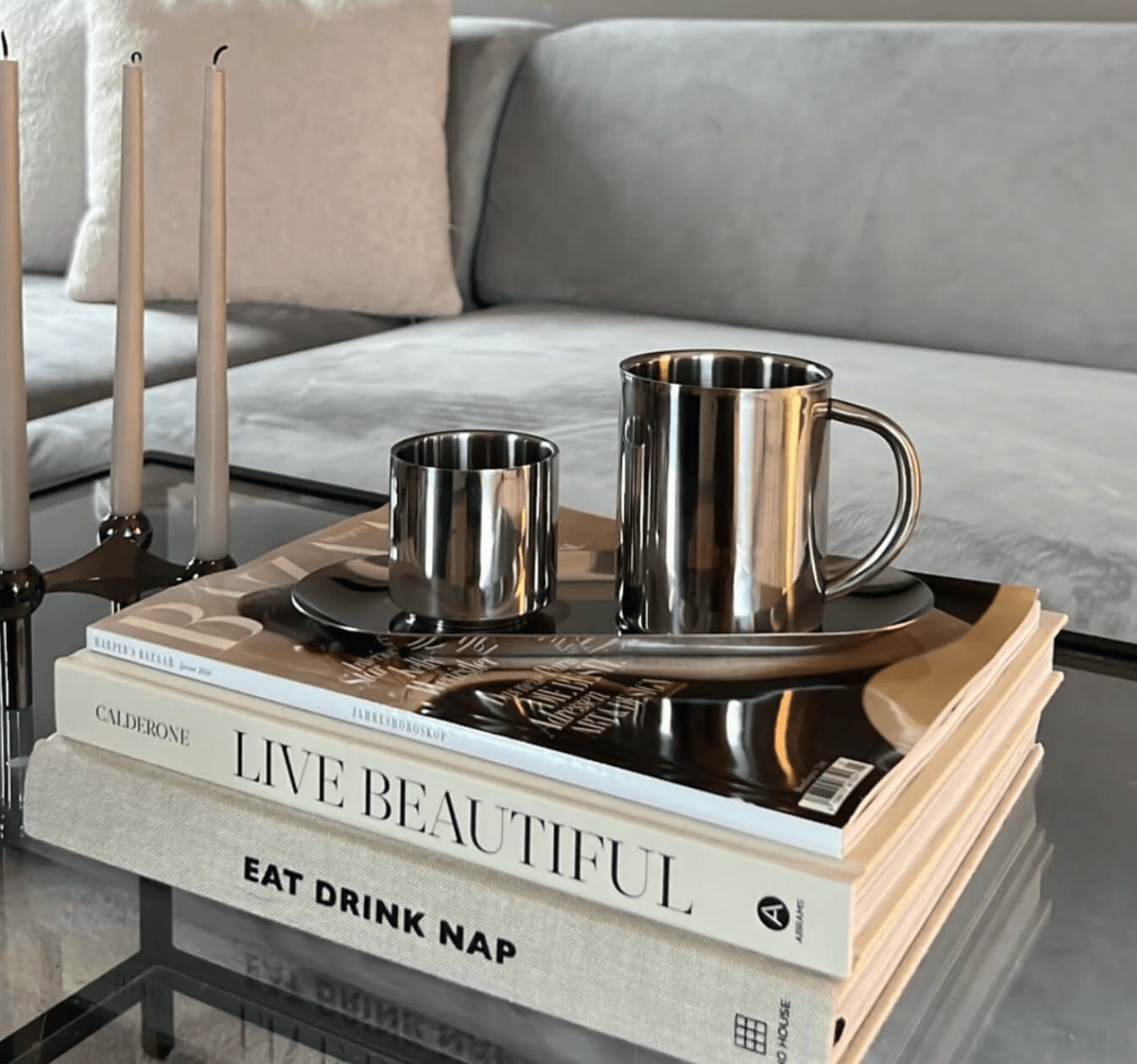 Minimalist stainless steel cups on a stack of stylish books on a glass coffee table, epitomizing modern luxury.