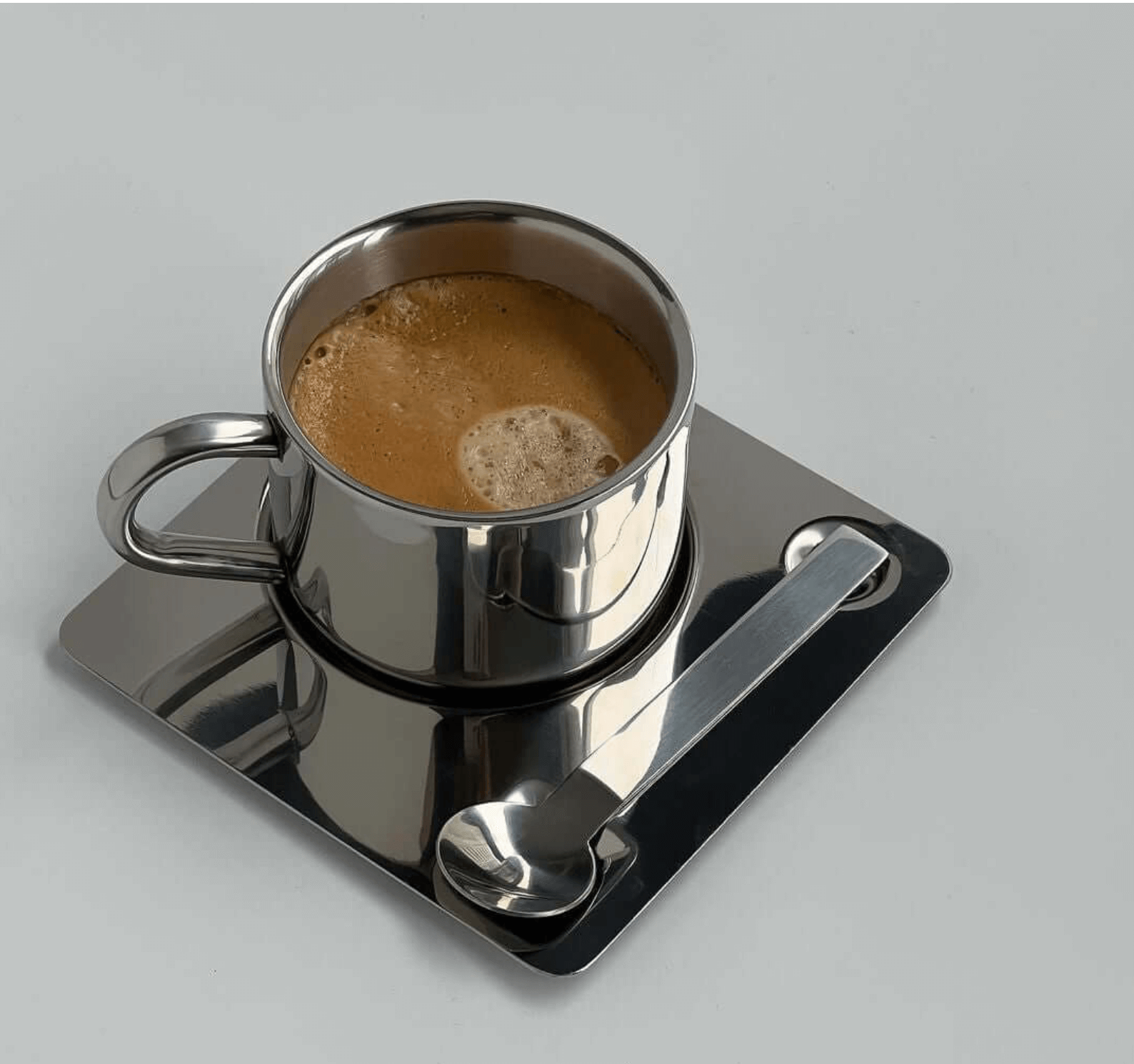Eckiges Edelstahl-Kaffeeset mit doppelwandiger Tasse und Löffel präsentiert auf einer quadratischen Untertasse.