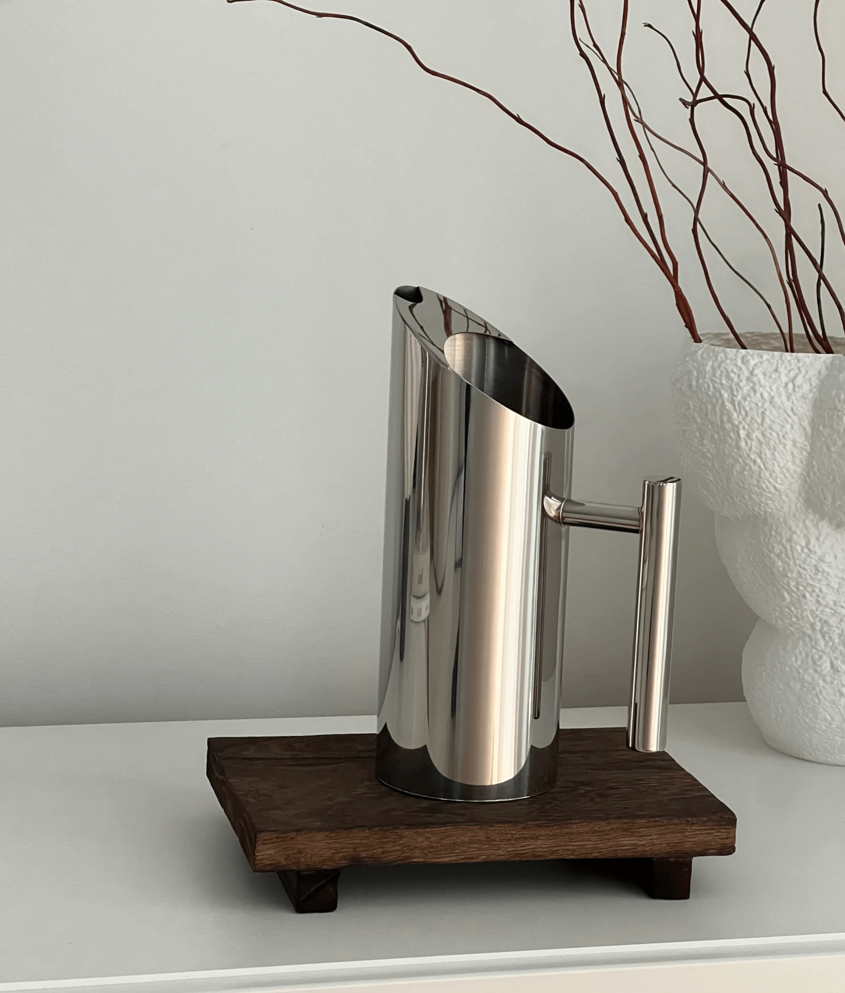 Edelstahl-Wasserkanne auf Holztablett, modernes Design für Tisch und Alltag, reflektierende Oberfläche, minimalistische Dekoration.