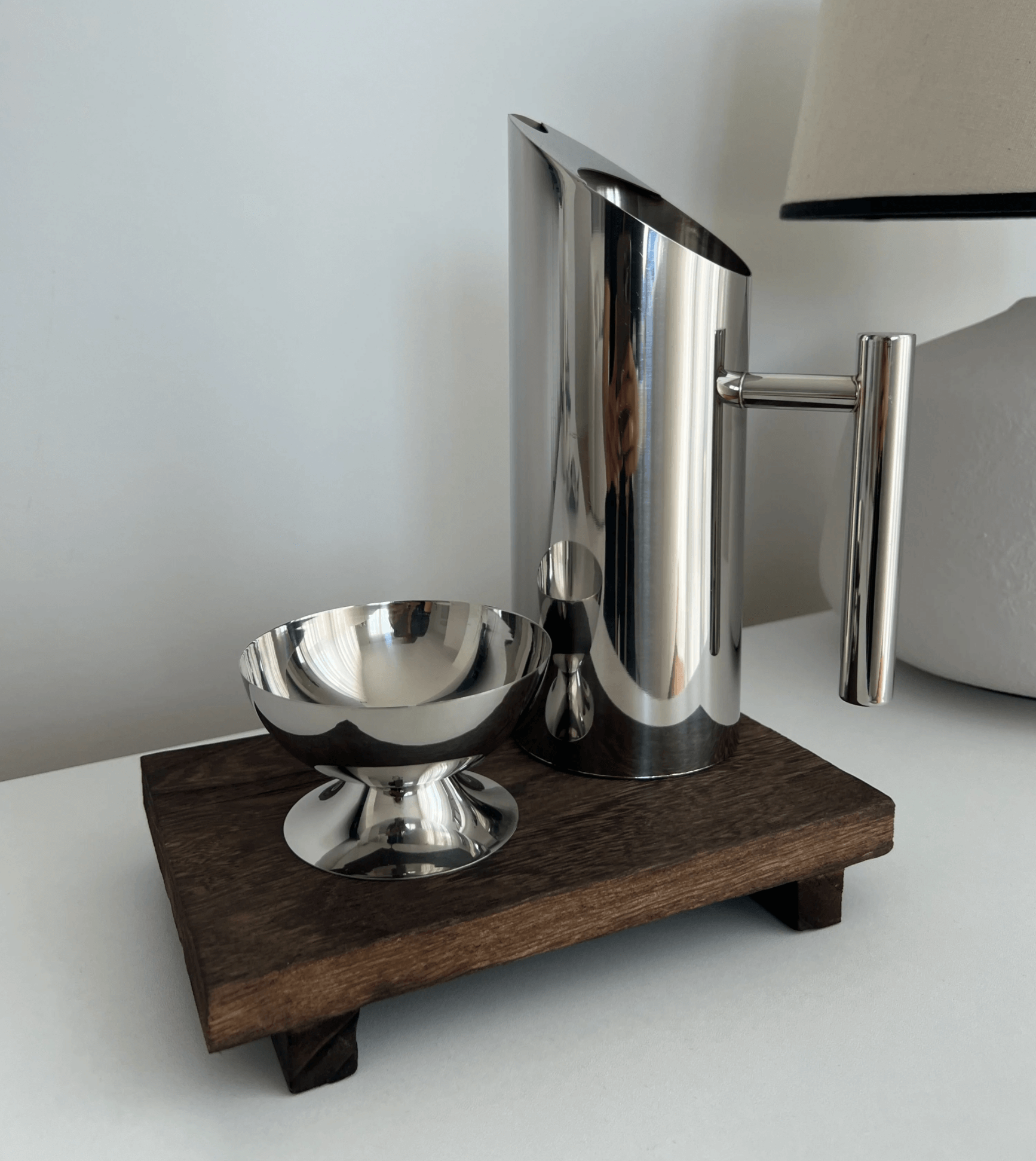 Stainless steel water jug on wooden stand with matching cup, showcasing modern design for everyday use and entertaining.