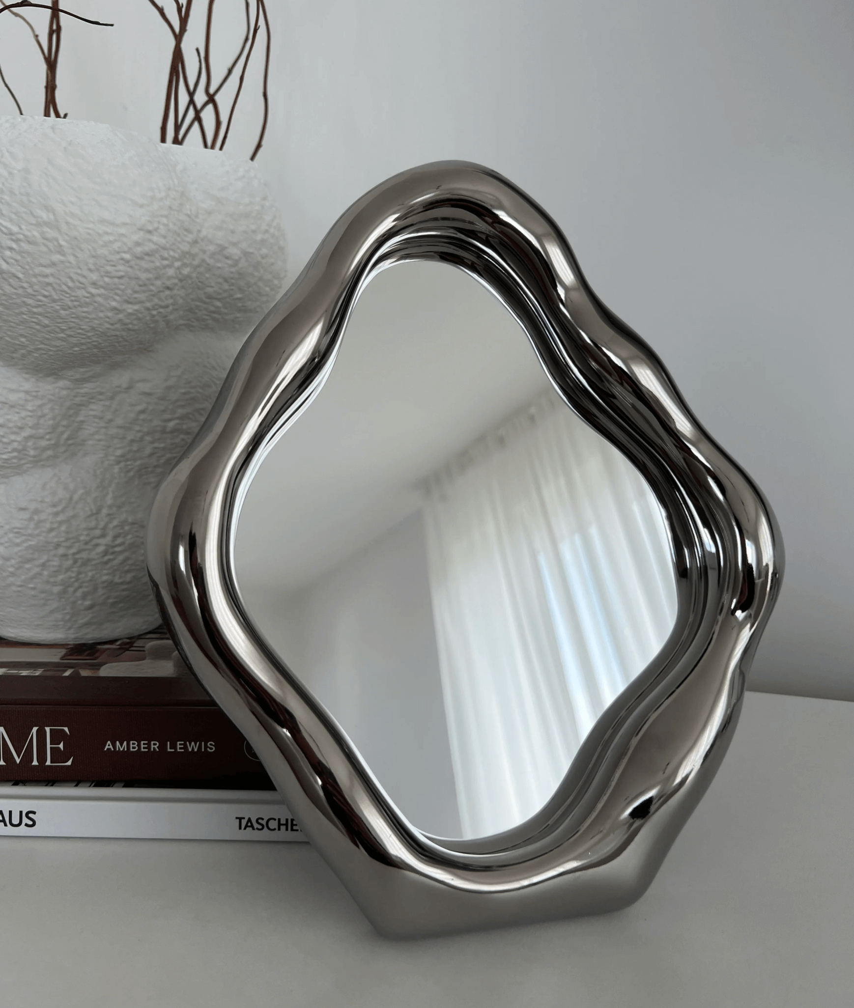 Elegant freestanding table mirror with stylish ceramic frame, reflecting natural light, placed next to modern decor.