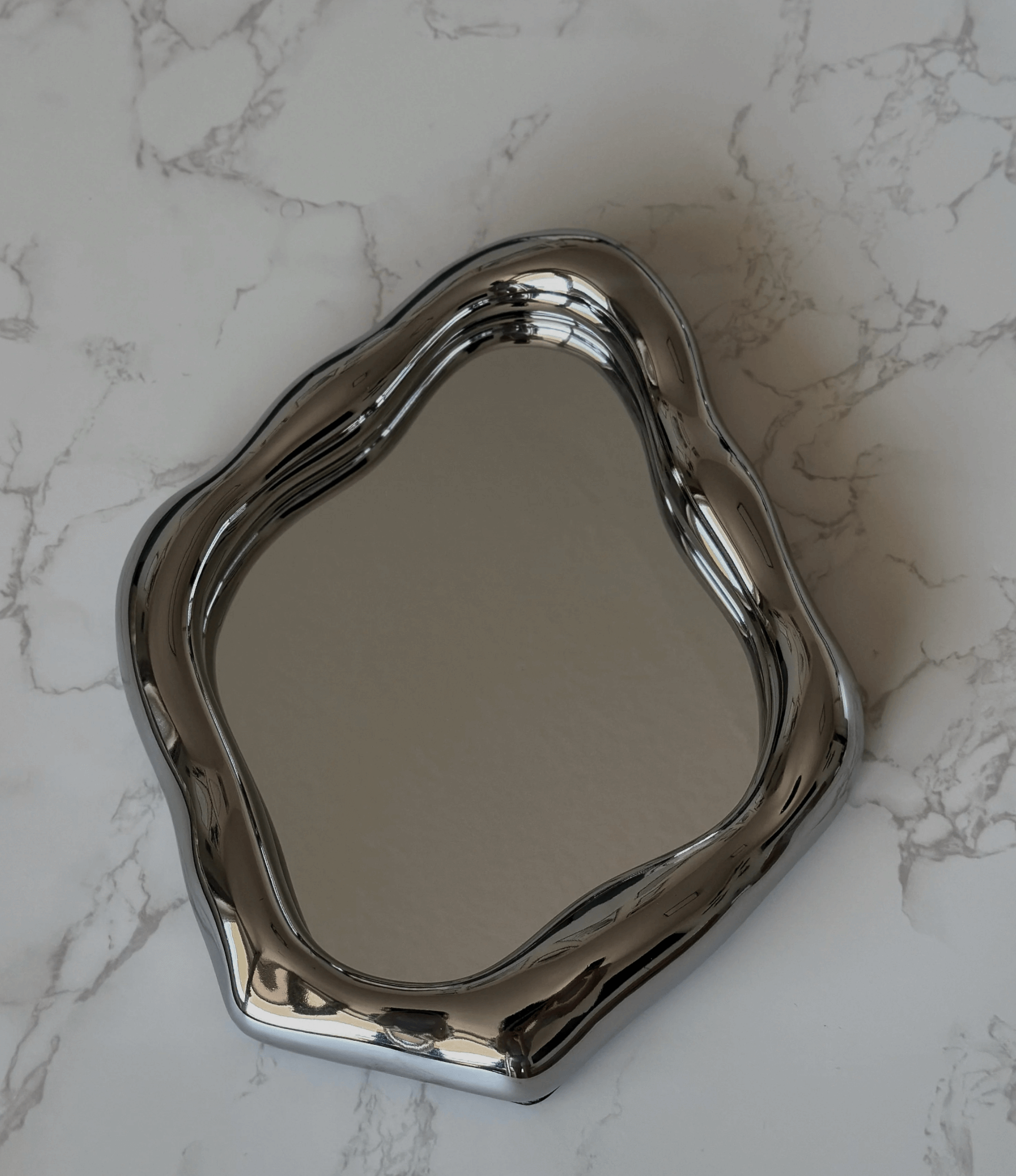 Elegant freestanding table mirror with wavy ceramic frame on marble surface, highlighting stylish design and functionality.